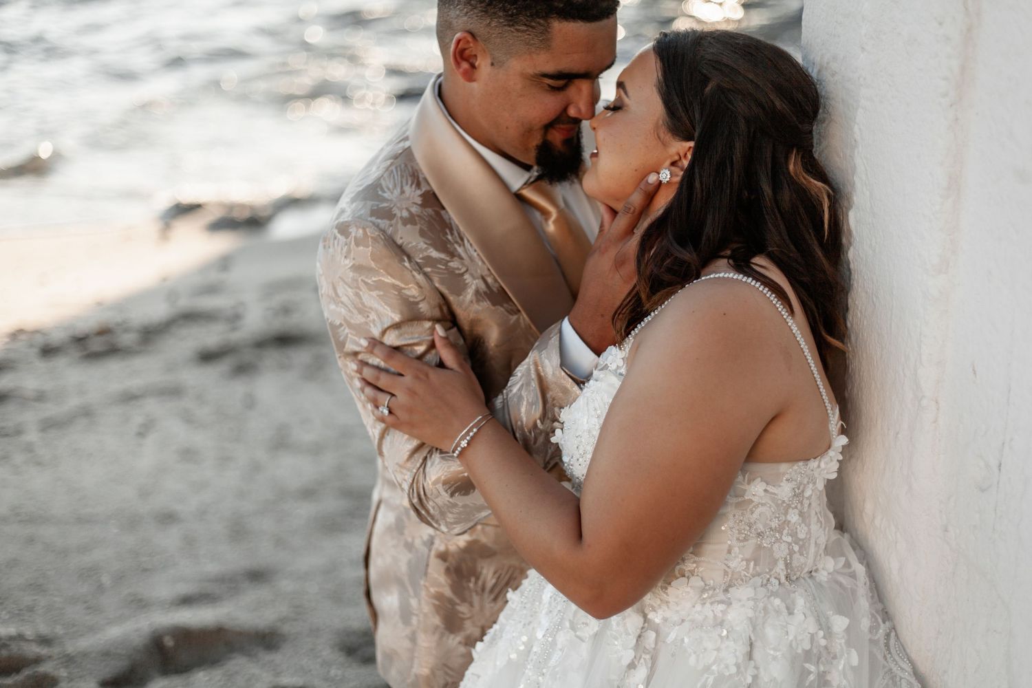 A couple embraces during a romantic beach wedding photoshoot with the groom wearing military fatigues and bride in white lace.