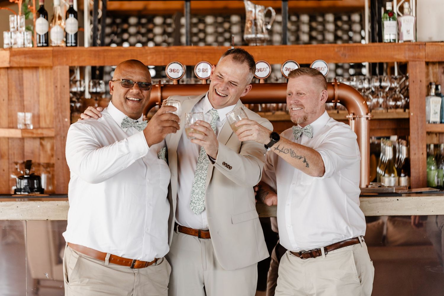A group of men stand at a bar counter in coordinated outfits of white shirts and khaki pants with brown belts.