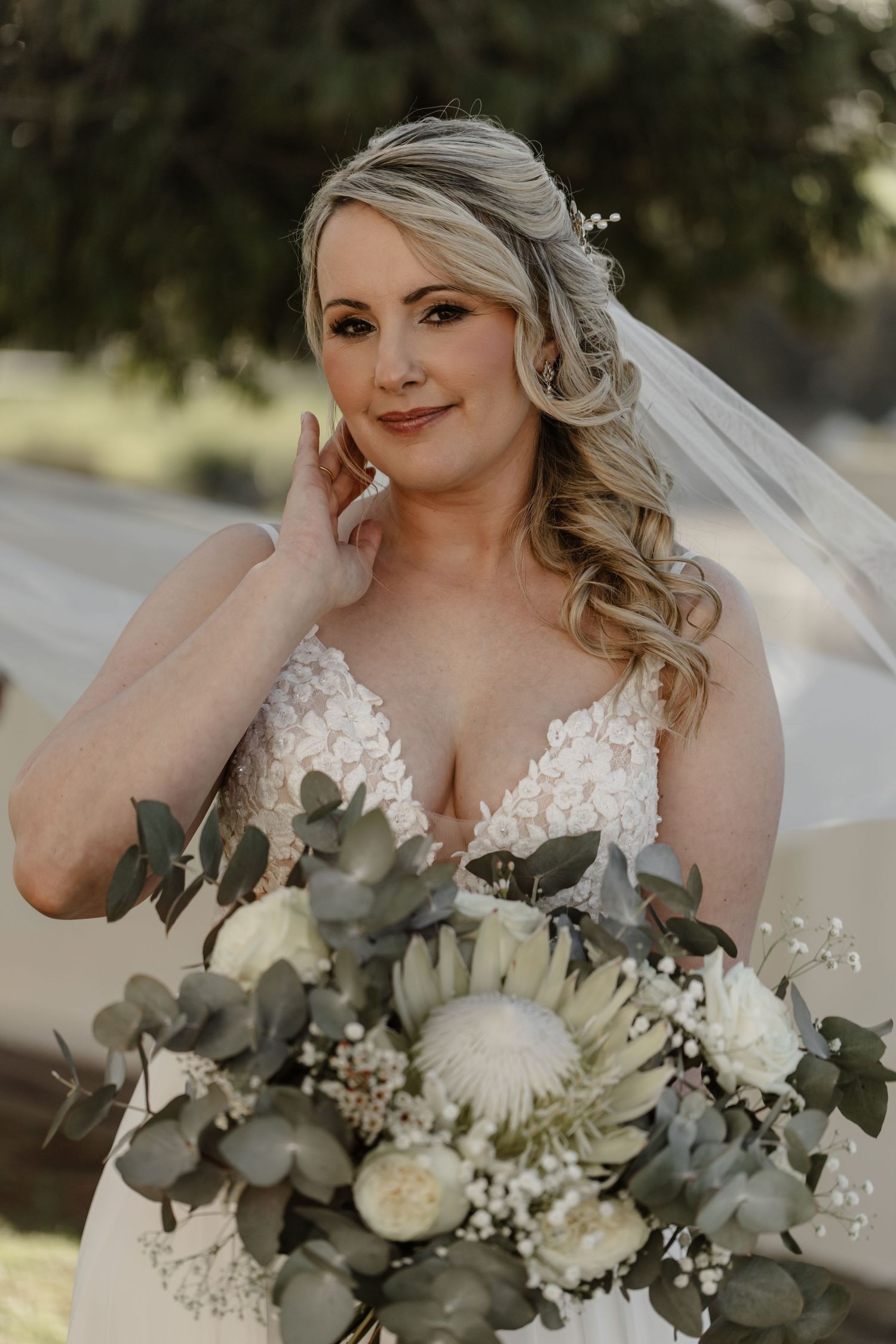 A bride in a lace wedding dress holds a stunning bouquet of white flowers and eucalyptus leaves on her wedding day.