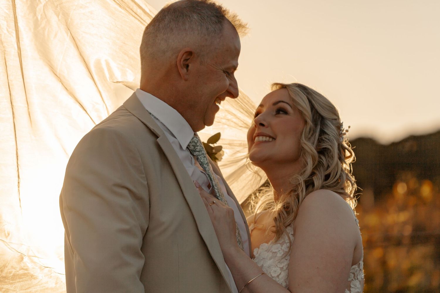 A couple shares a romantic moment during sunset, laughing together in their wedding attire.
