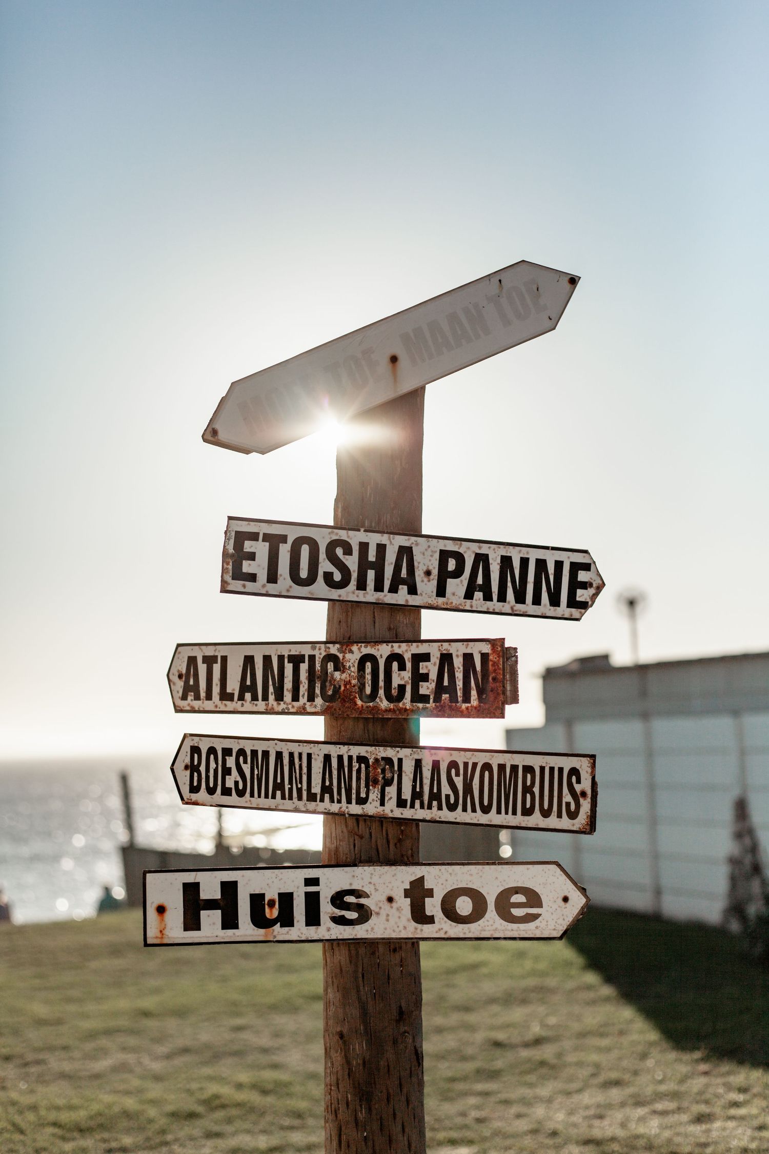 Rustic wooden directional sign post pointing to Etosha-Panne, Atlantic Ocean and other destinations with sun flare in background.