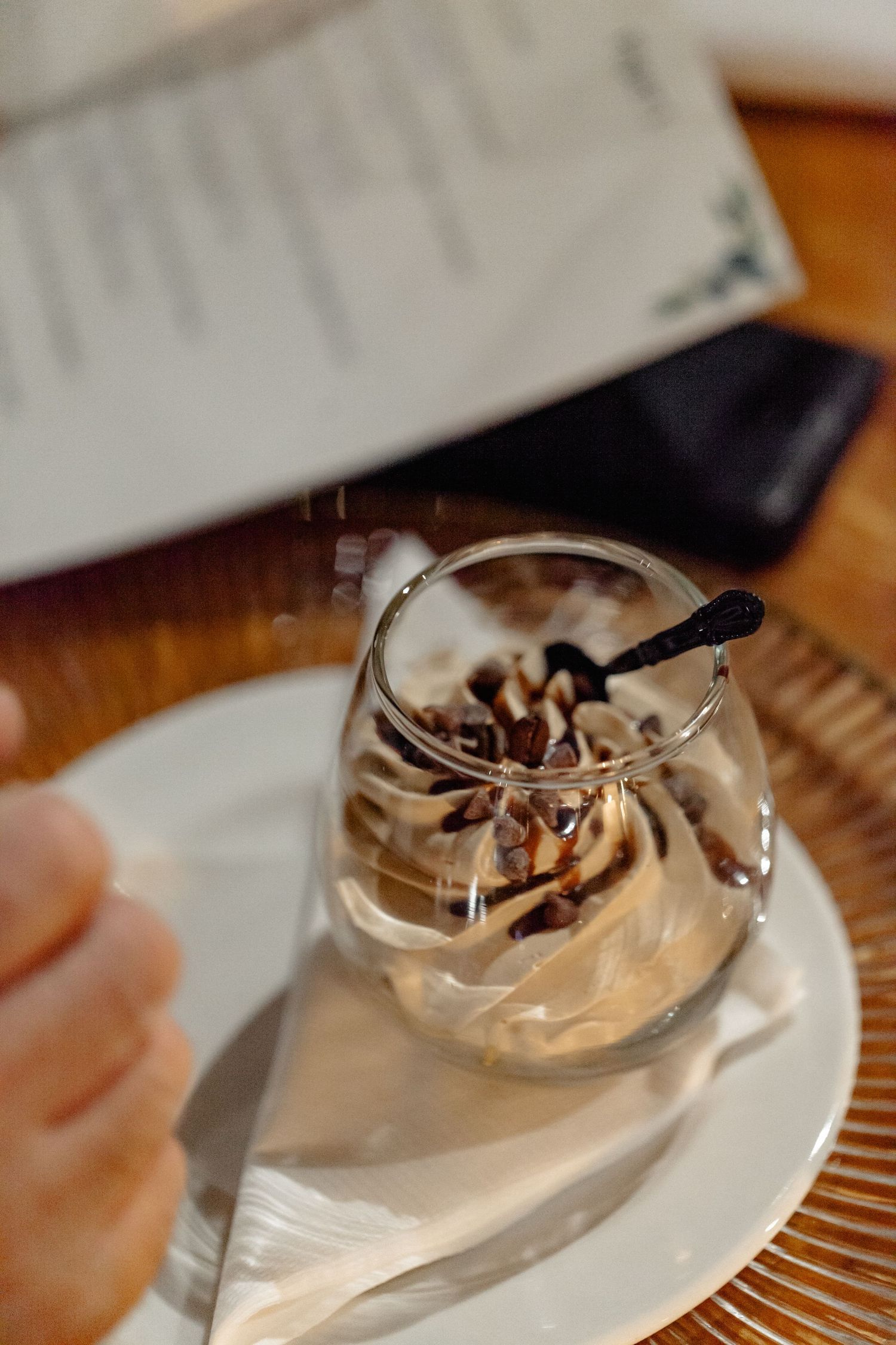 A creamy dessert served in a glass with chocolate drizzle and whipped topping on a white plate.