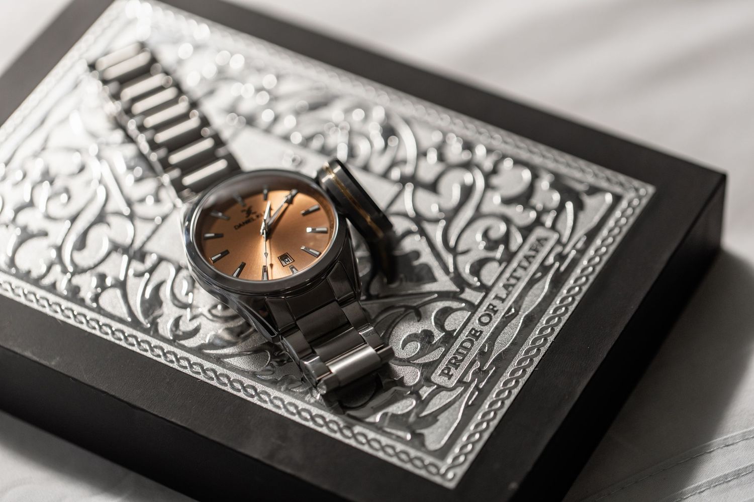 A stylish dark watch rests on a black and white decorative book cover with intricate patterns.