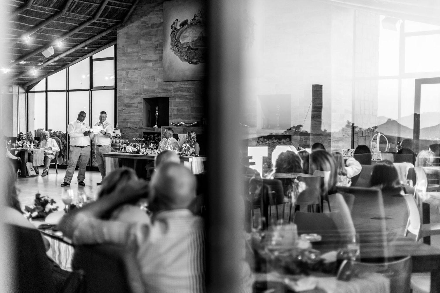 People relaxing in a food court mall area with white tables and chairs visible in a black and white photograph.