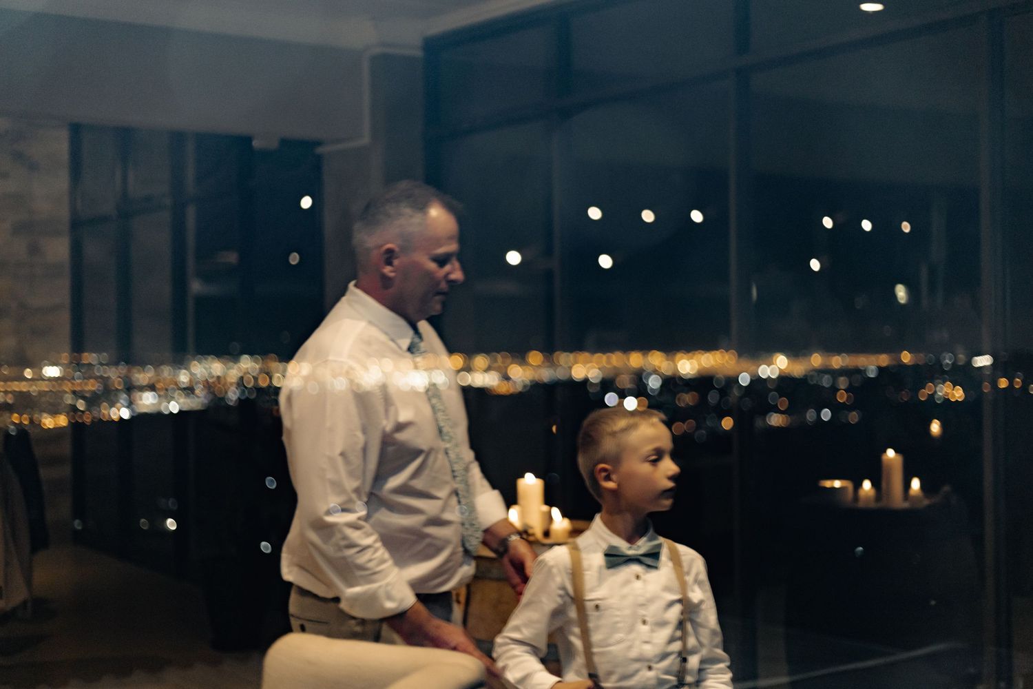 Two people stand together looking at a city skyline at night through large windows.