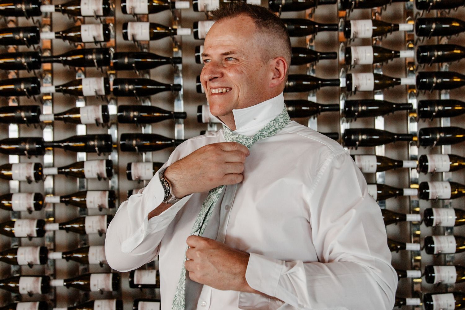 Someone adjusts a mint green bowtie while standing in front of a wall of wine bottles.