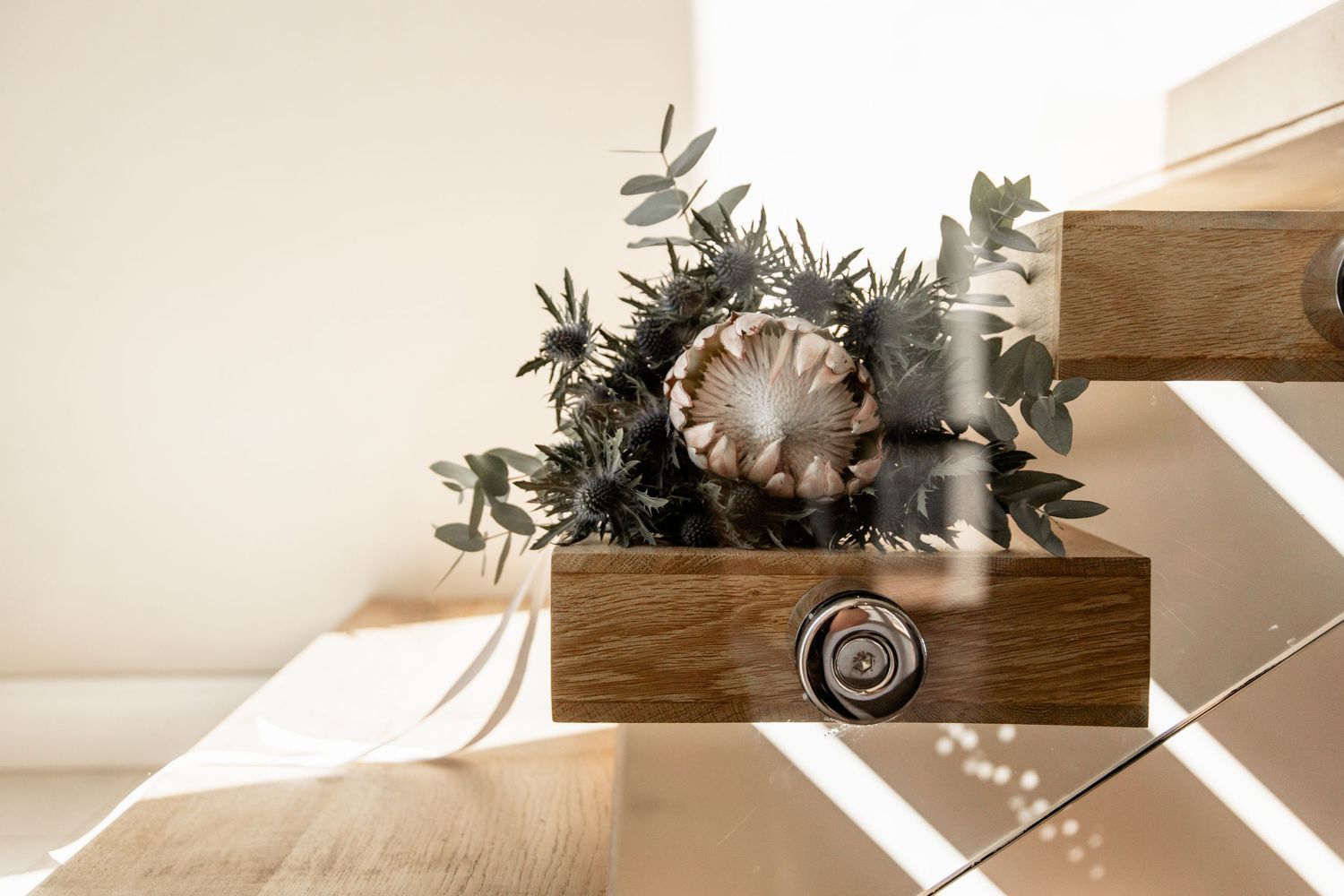 Rustic wooden box with eucalyptus leaves and dried floral arrangement sitting on wooden surface in natural sunlight.
