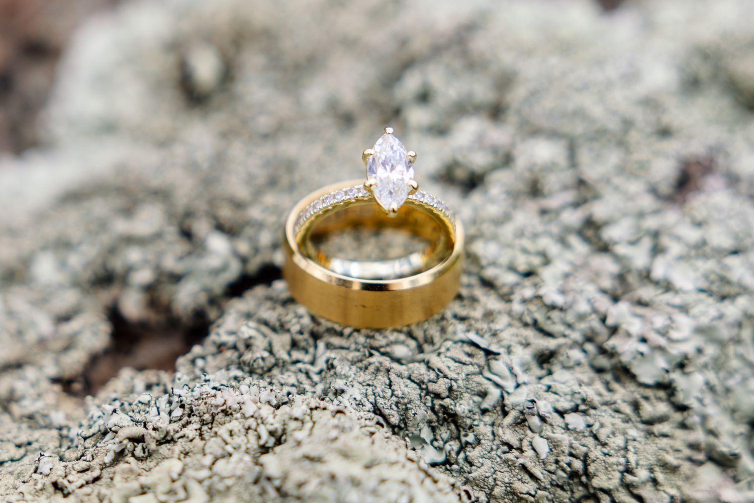 Gold wedding band with diamond solitaire on gray stone surface glimmers in natural light.