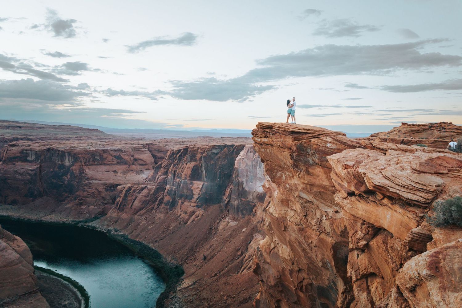 A romantic moment captured on the edge of a massive canyon cliff at sunset.