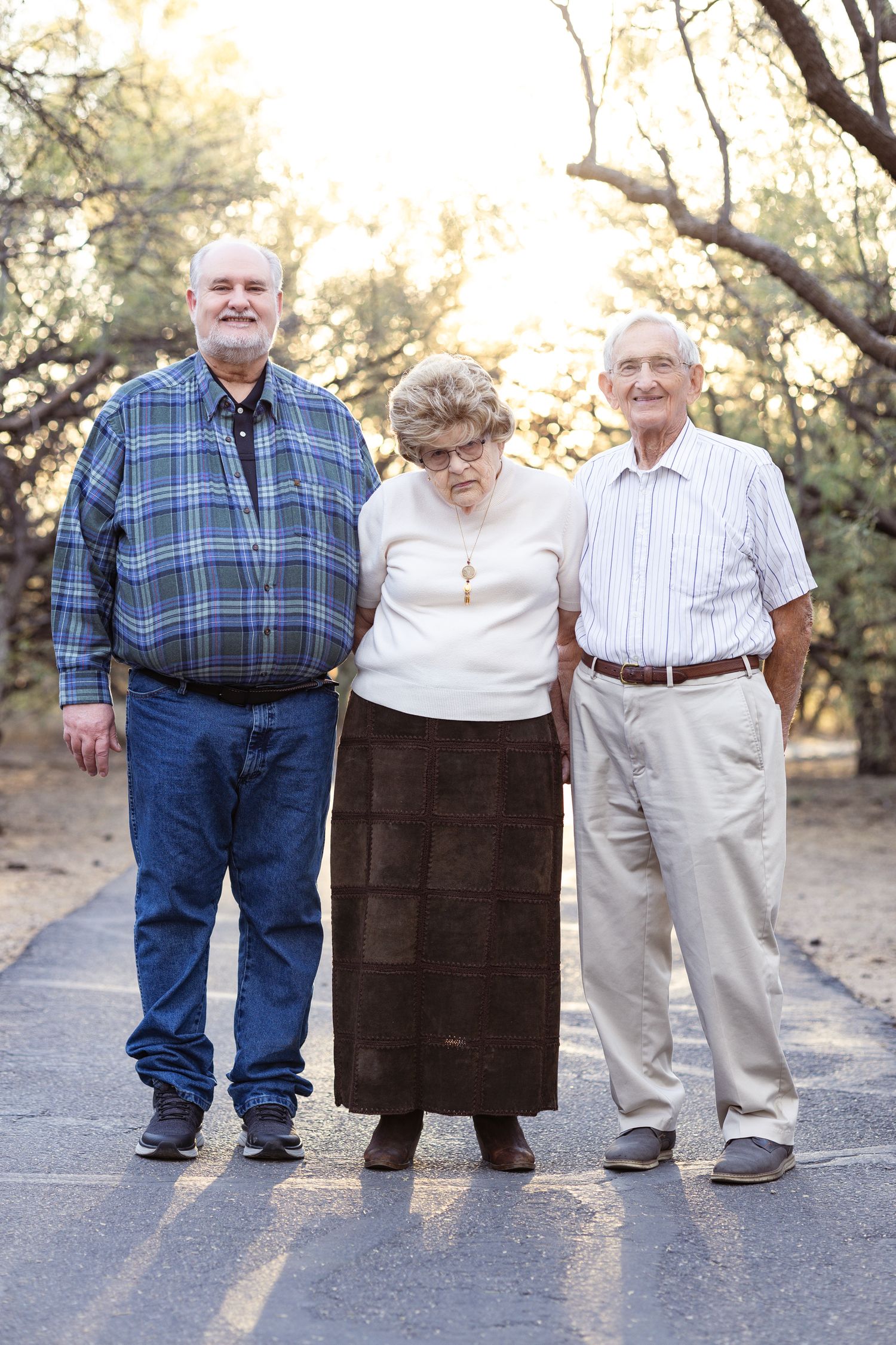 Three people stand together on a path at sunset wearing casual clothing.