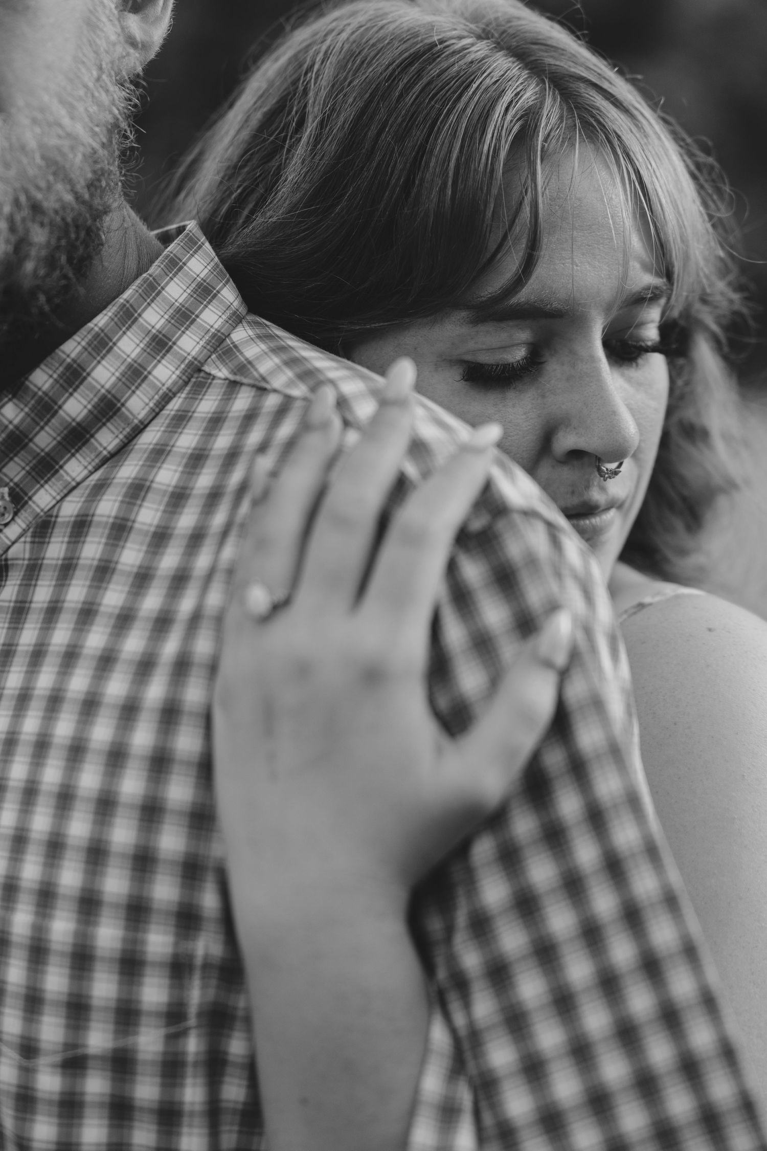 Black and white romantic portrait showing a tender embrace against a plaid shirt with eyes closed in an intimate moment.