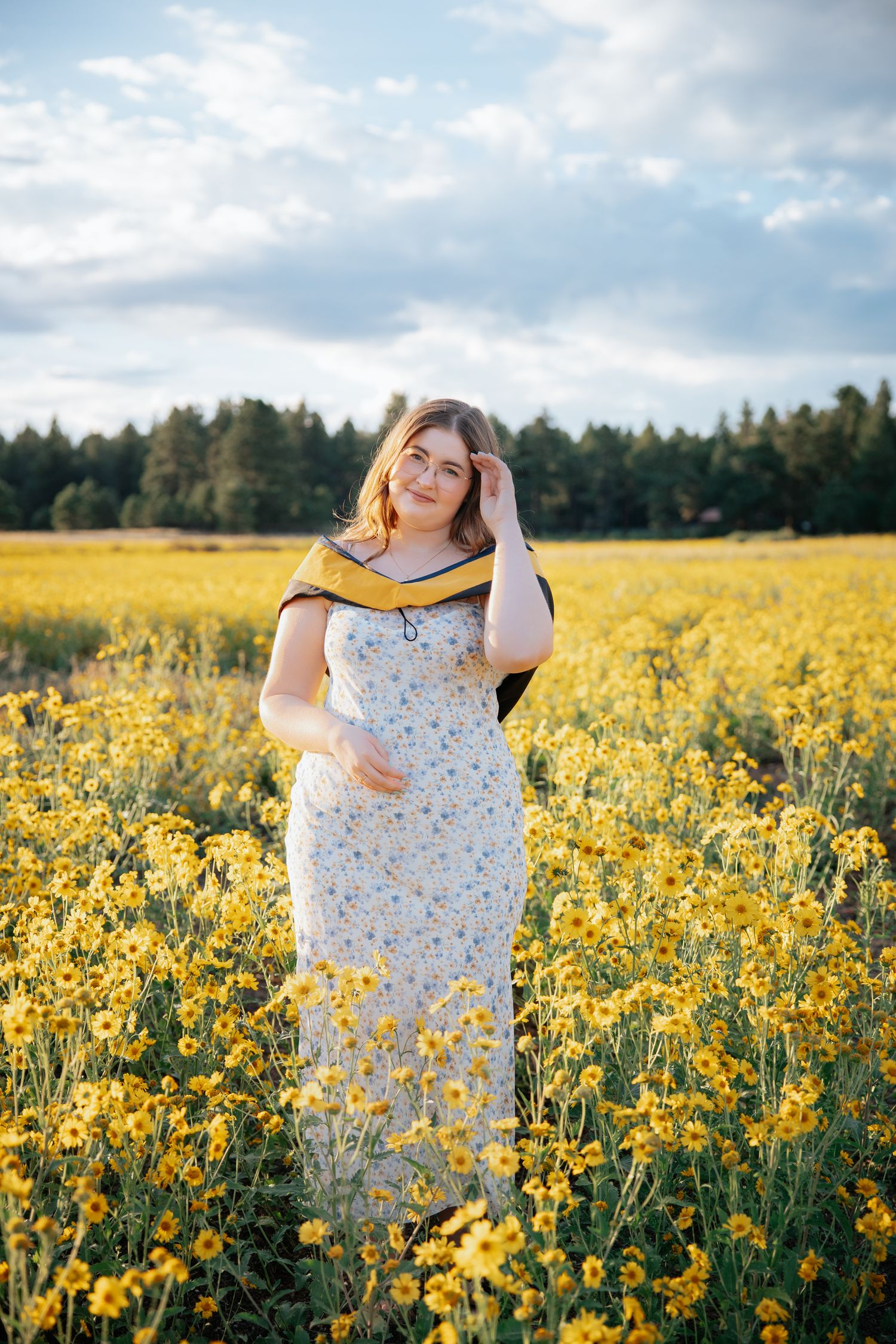 A woman in a floral dress is standing in a vibrant field of yellow wildflowers on a sunny summer day.