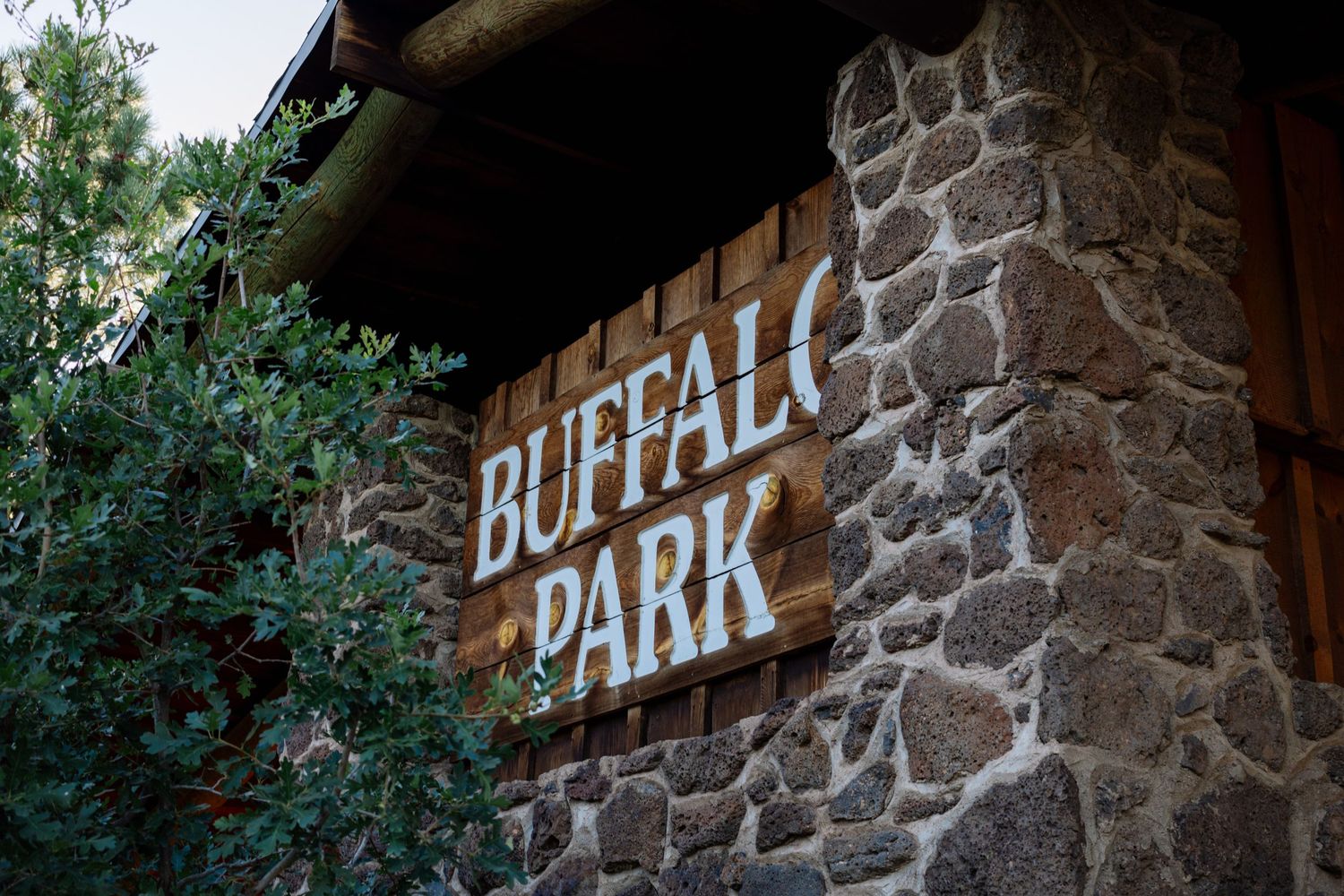 Stone wall entrance with rustic 'Buffalo Park' signage mounted on textured stonework beside green foliage.