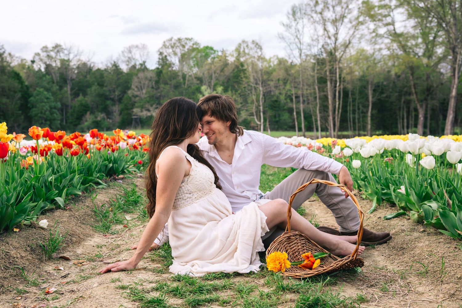 A romantic springtime scene with a couple sitting on a blanket surrounded by vibrant red and yellow tulips in bloom.