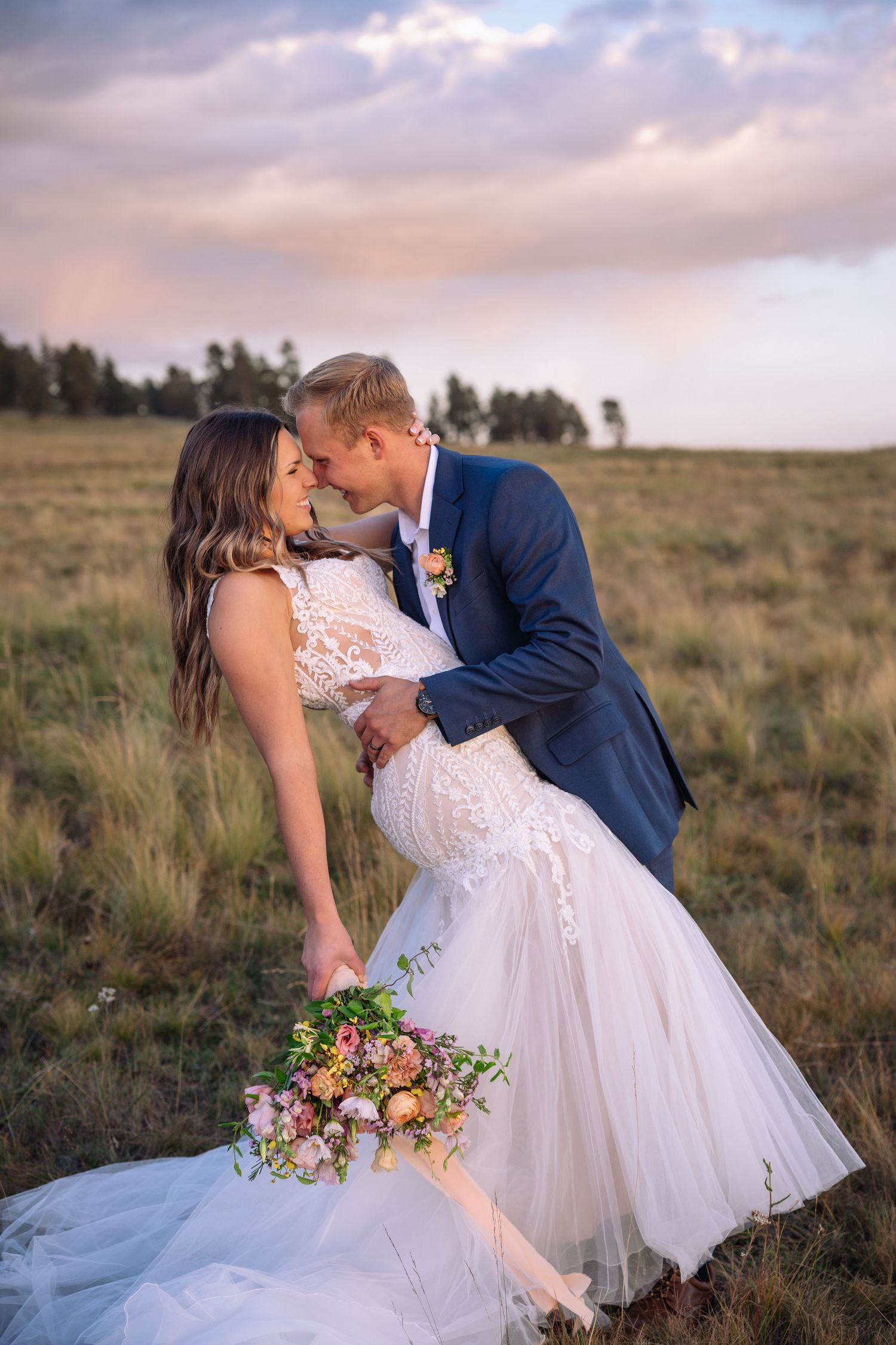 Romantic wedding photo in an open field at sunset with a beautiful white lace dress and colorful bouquet.