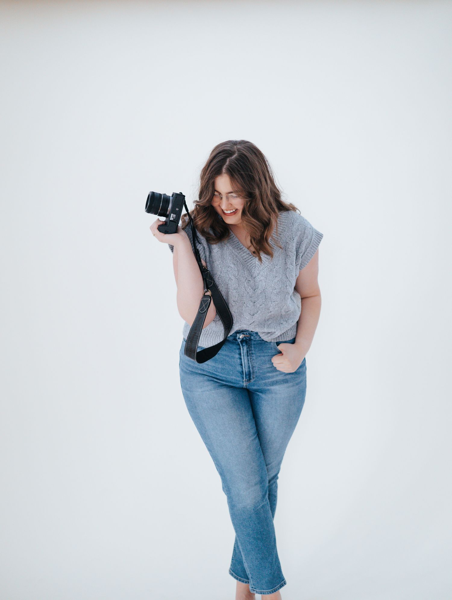 A Tennessee photographer in a gray shirt and jeans poses with a camera against a white backdrop.