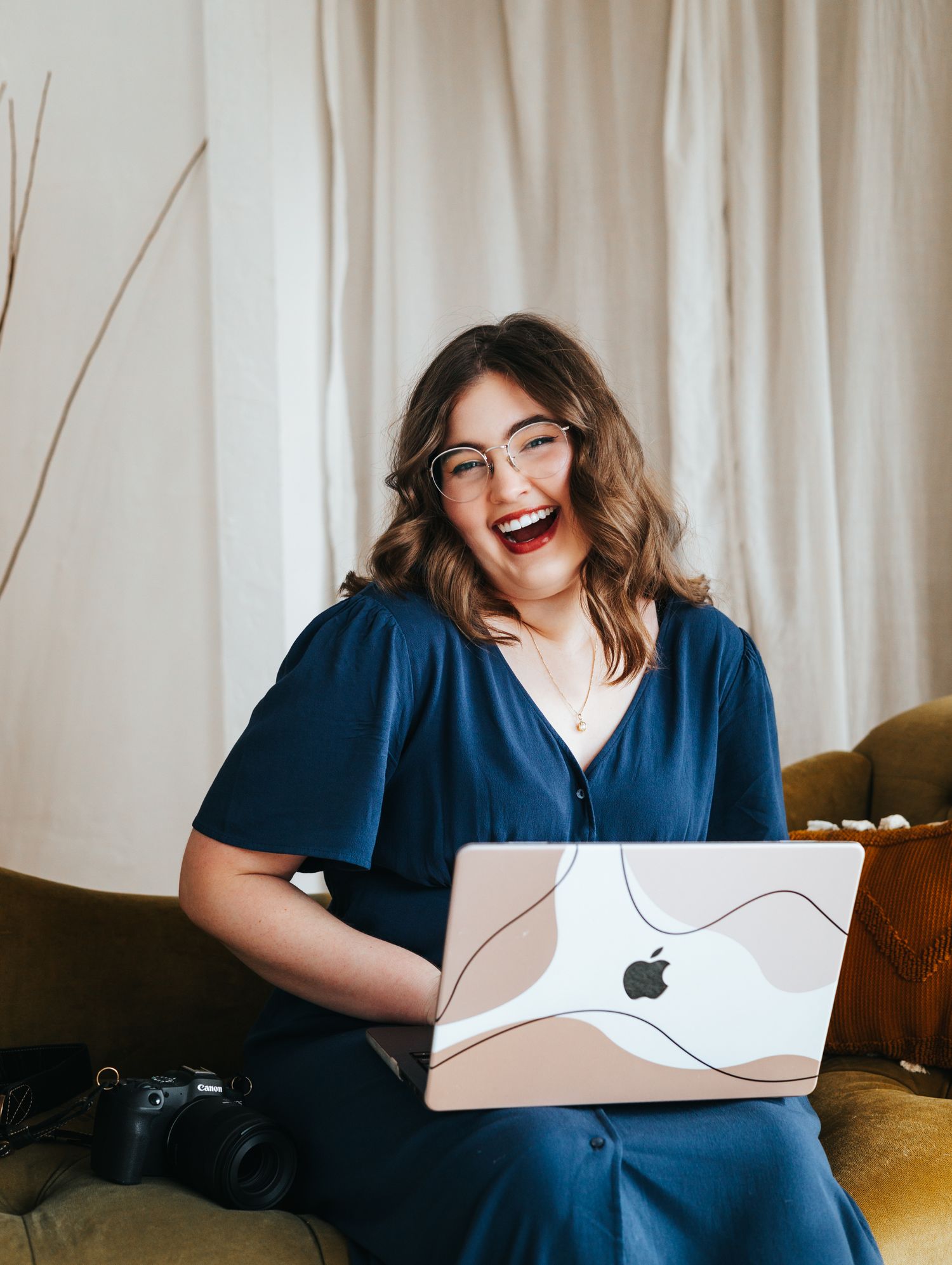 Bethany a creative professional works on laptop while seated on couch in navy blue dress.