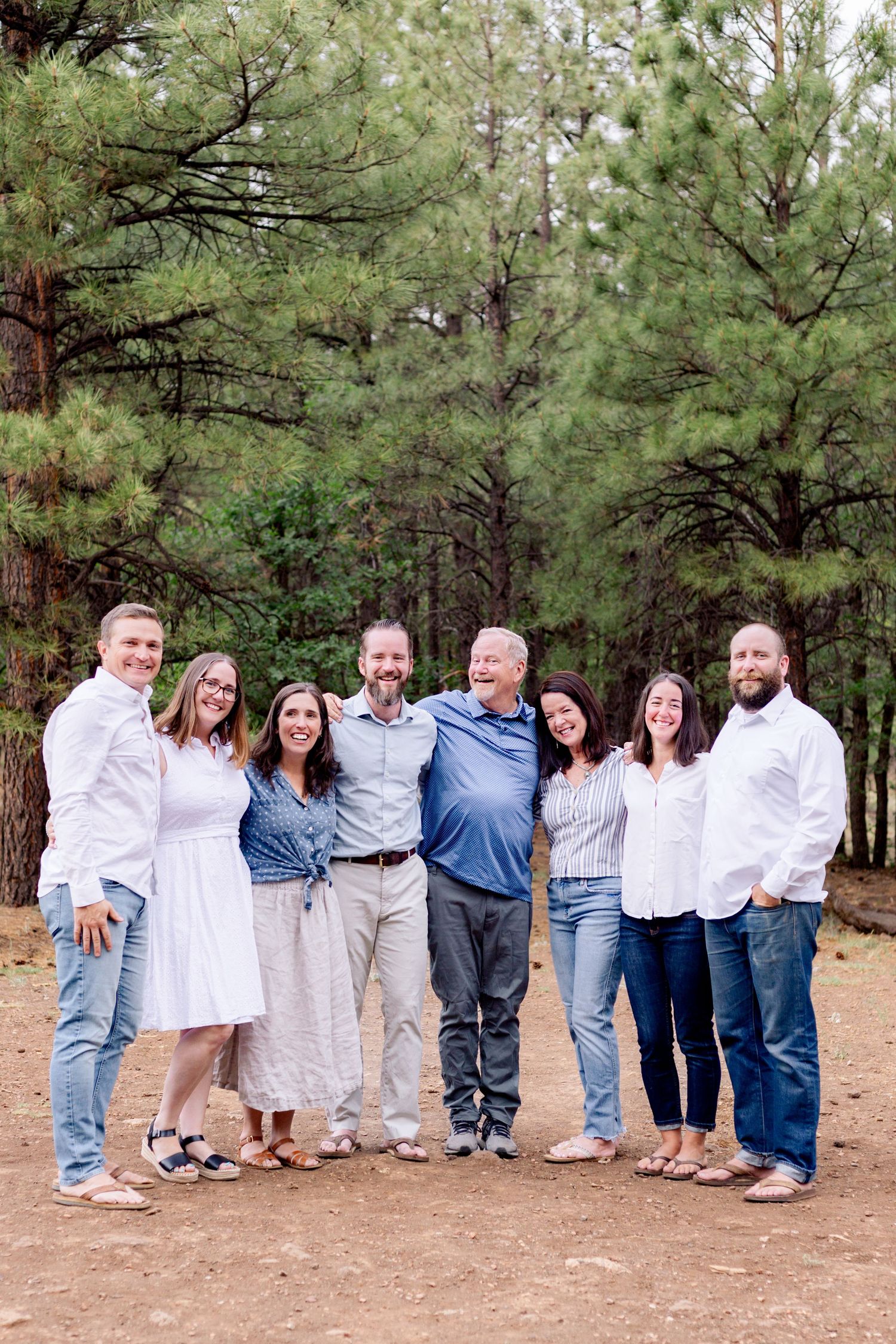 Family group portrait standing together on dirt path surrounded by tall pine trees.