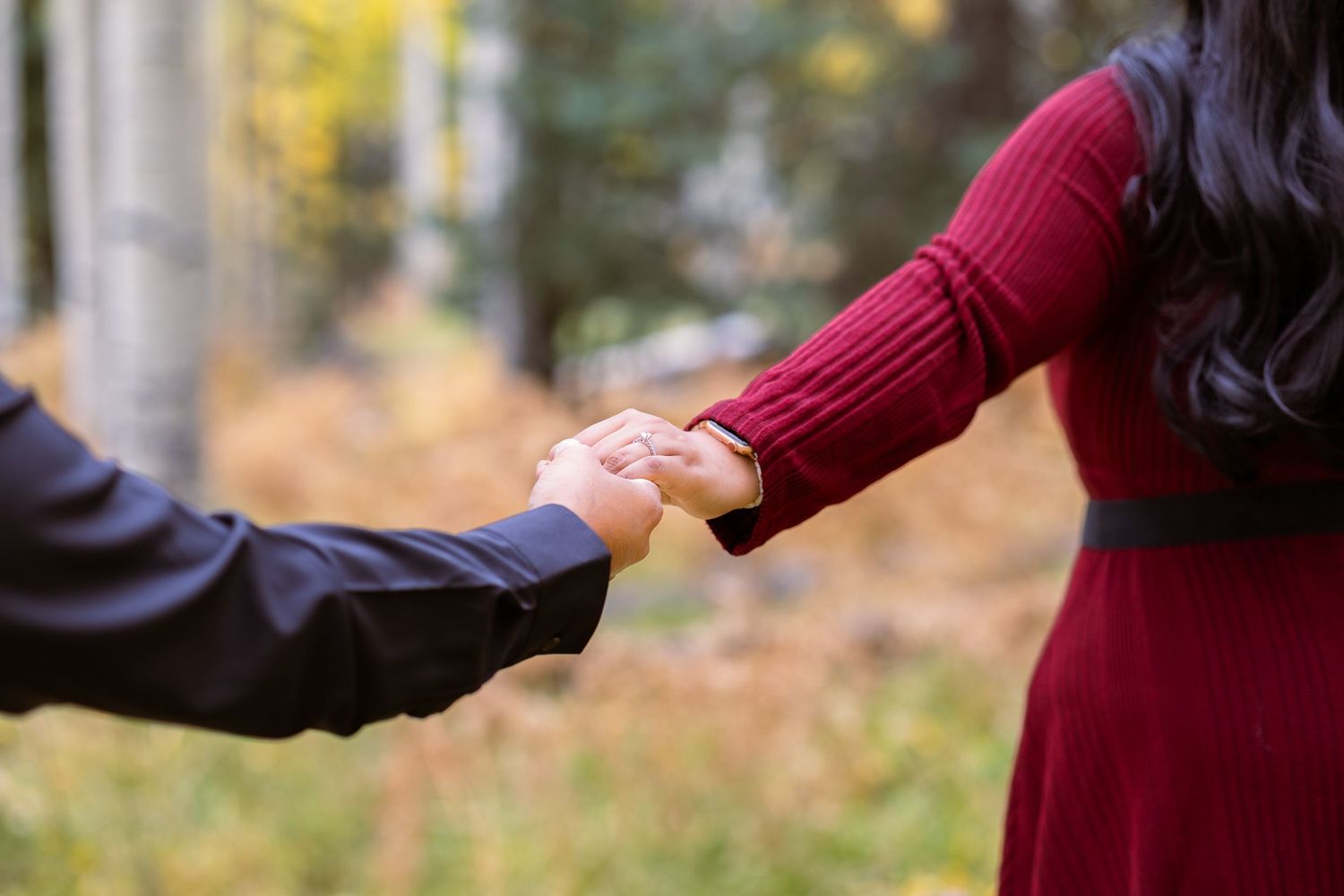 Two hands clasped together in autumn, one wearing burgundy and one wearing navy sleeves.