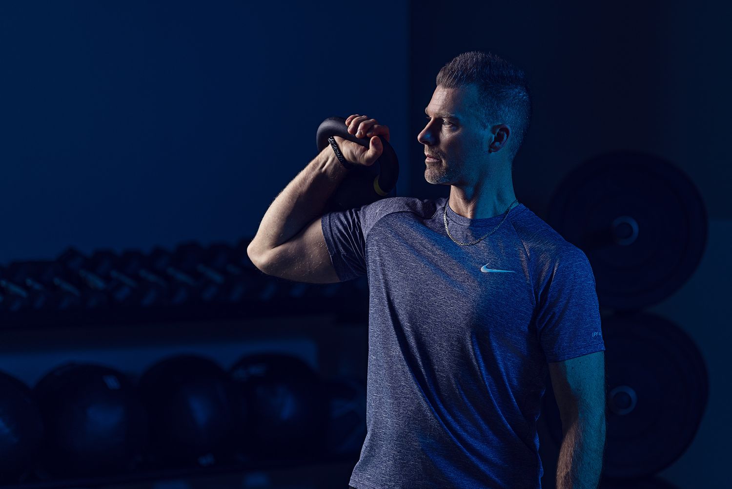 Dramatic side-lit fitness portrait against dark background with exercise equipment.