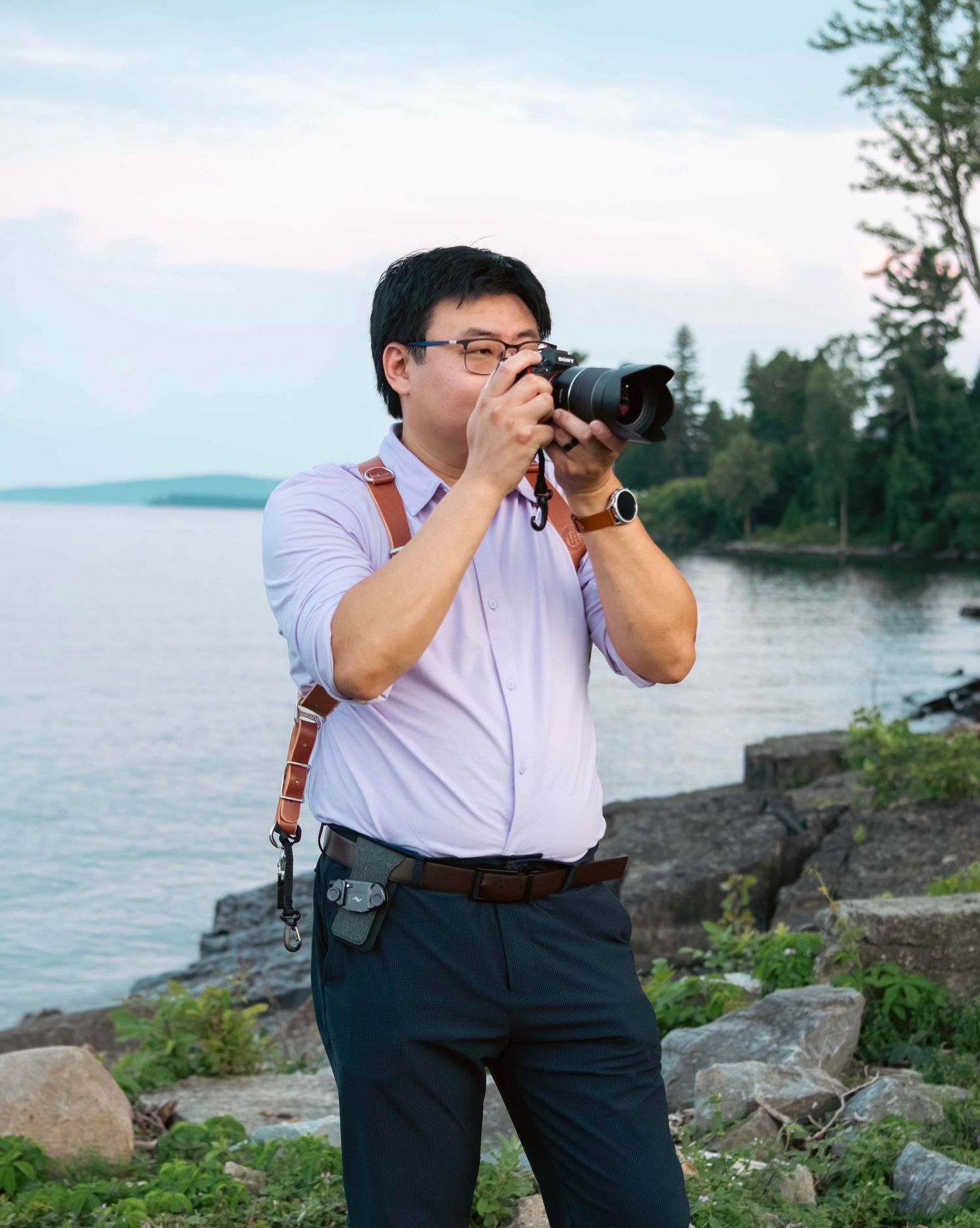 Photographer in pink shirt captures images along scenic coastal shoreline.