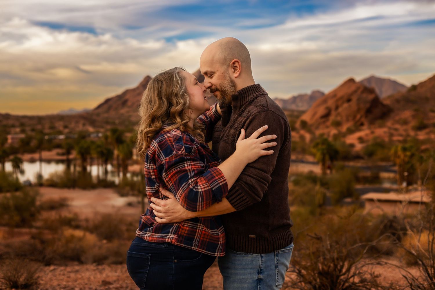 A couple embraces during sunset at Papago Park in Phoenix with red rock formations and desert landscape in background.
