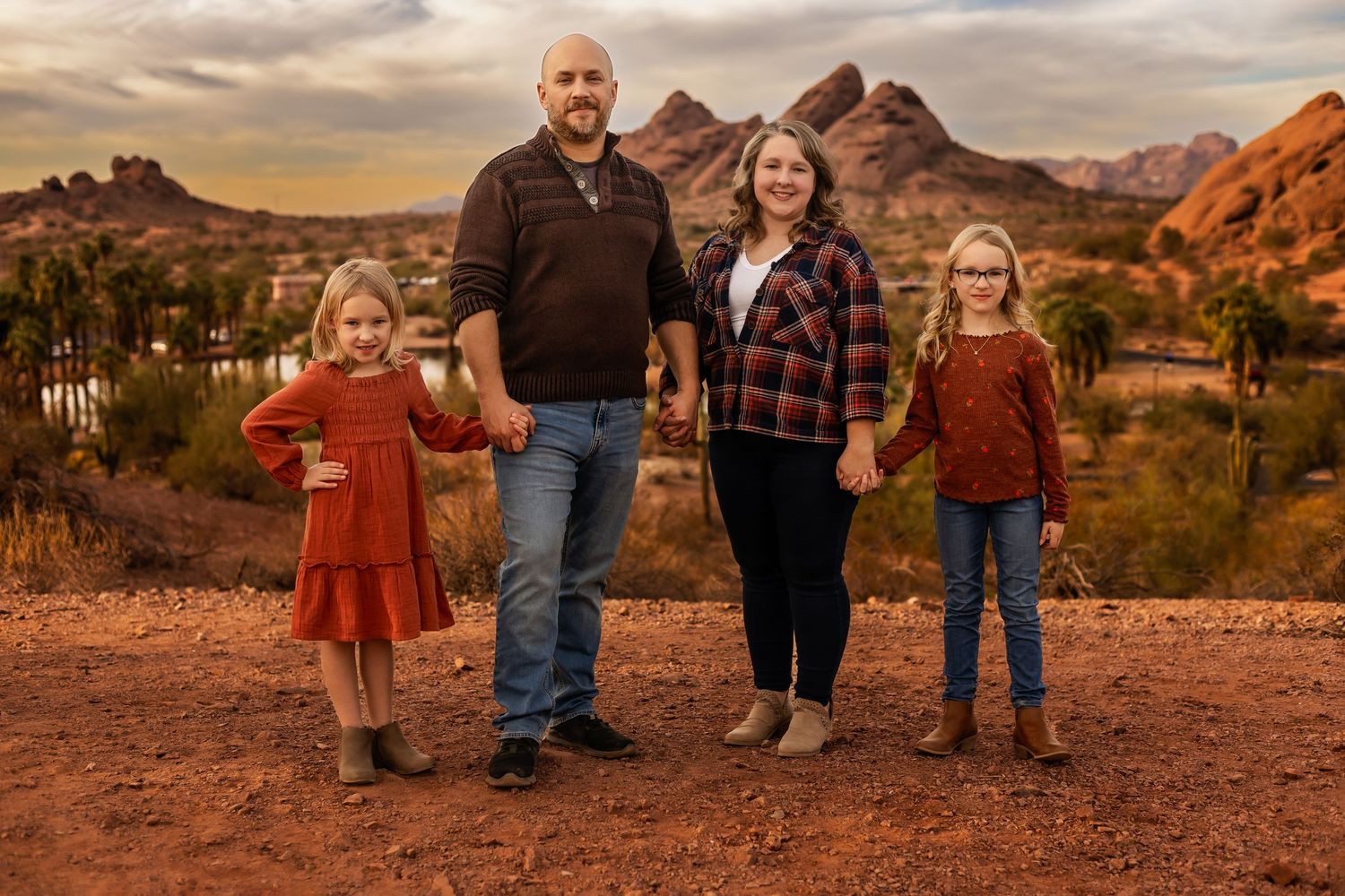 A family poses together against a backdrop of red desert rock formations at sunset in Arches National Park.