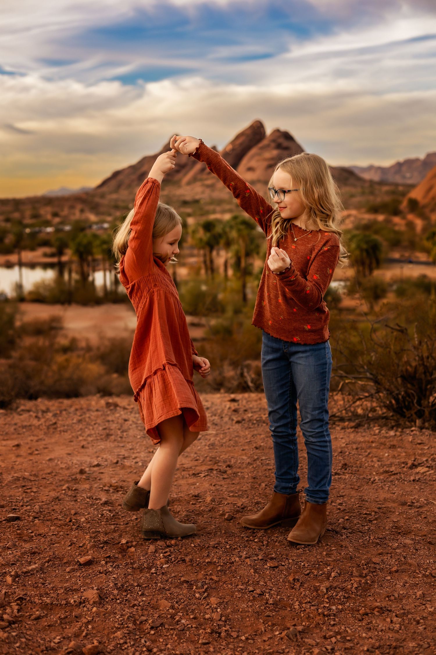 Two people dancing together at sunset in the desert with red rocks and mountains in the background.