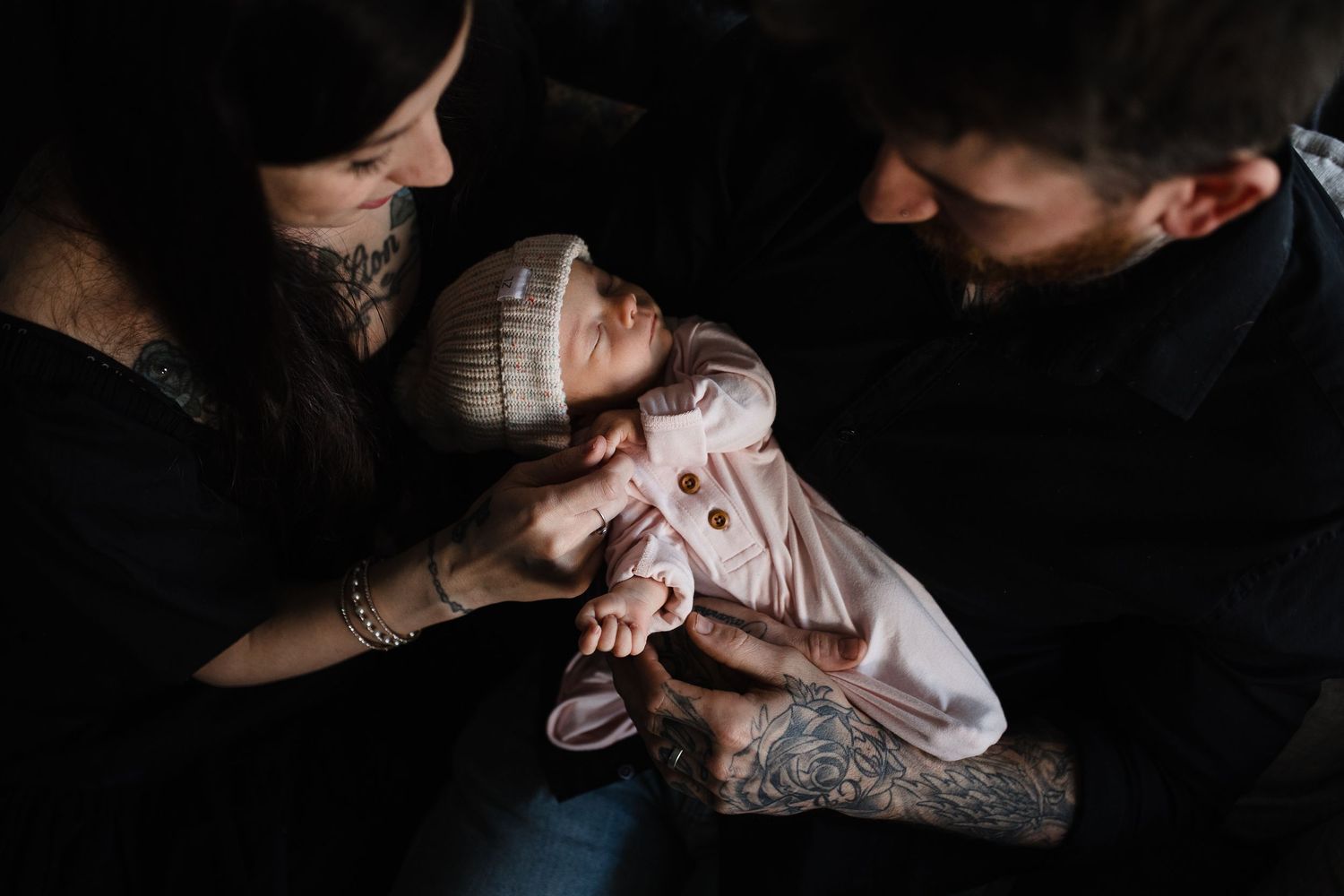 Parents tenderly care for their newborn baby wearing a knit hat in an intimate black and white portrait.