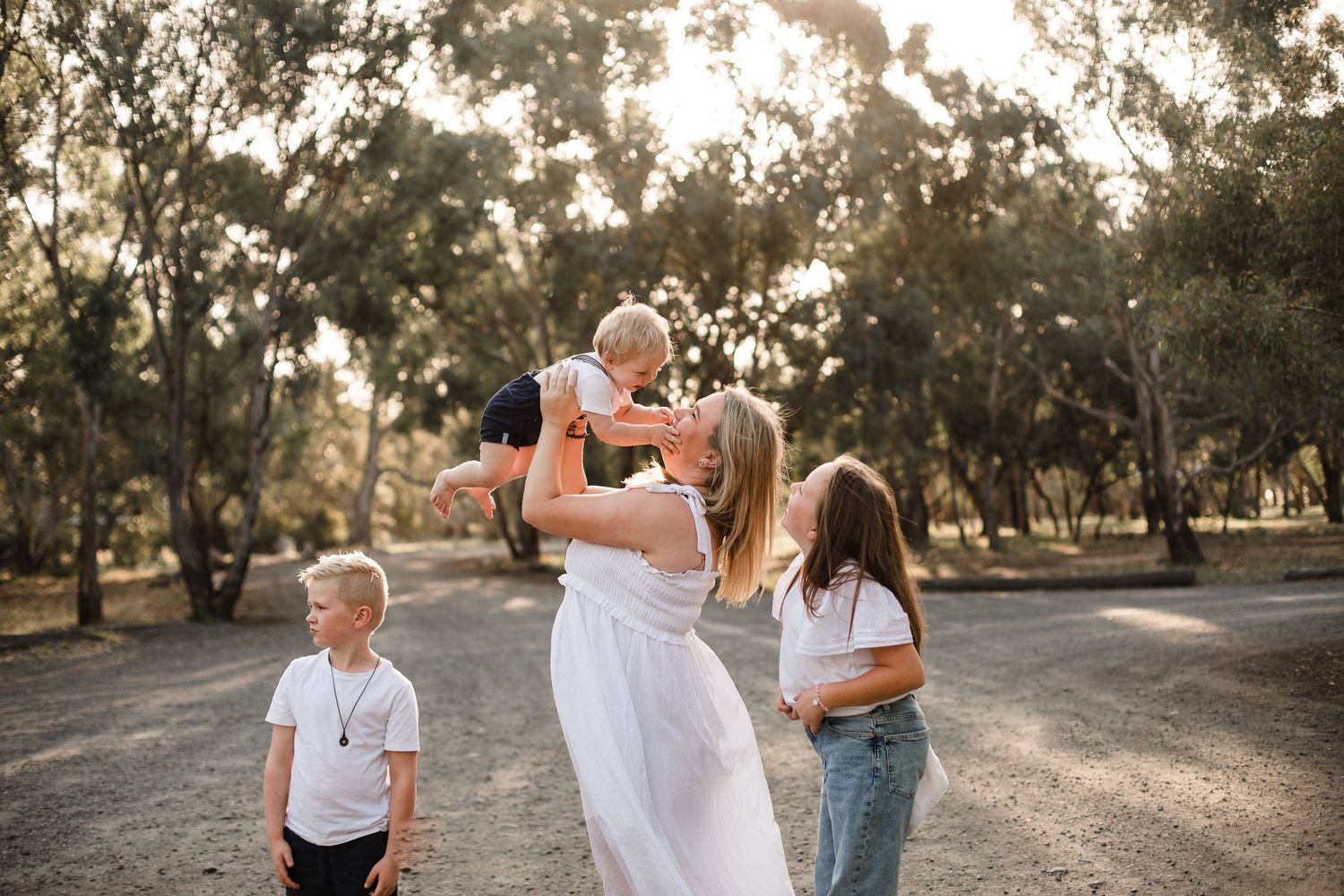 Family sharing a joyful moment together on a sunlit dirt path surrounded by trees at golden hour.