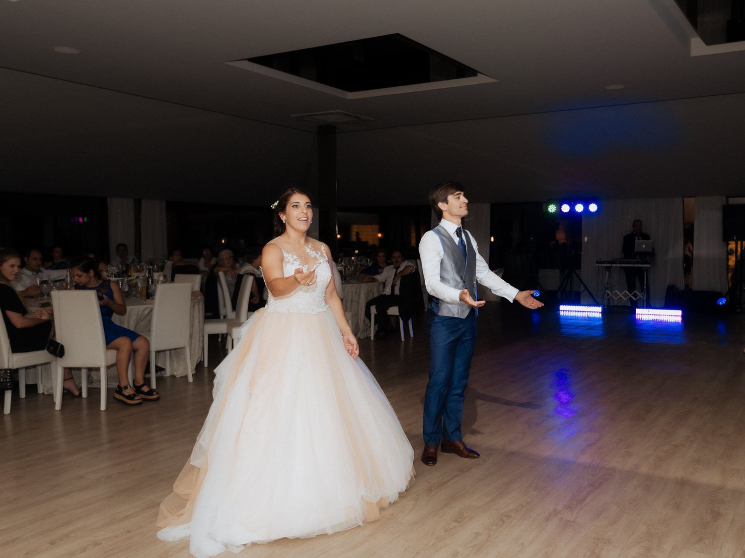 Two people dancing at a wedding reception on a wooden dance floor with blue lighting in the background.