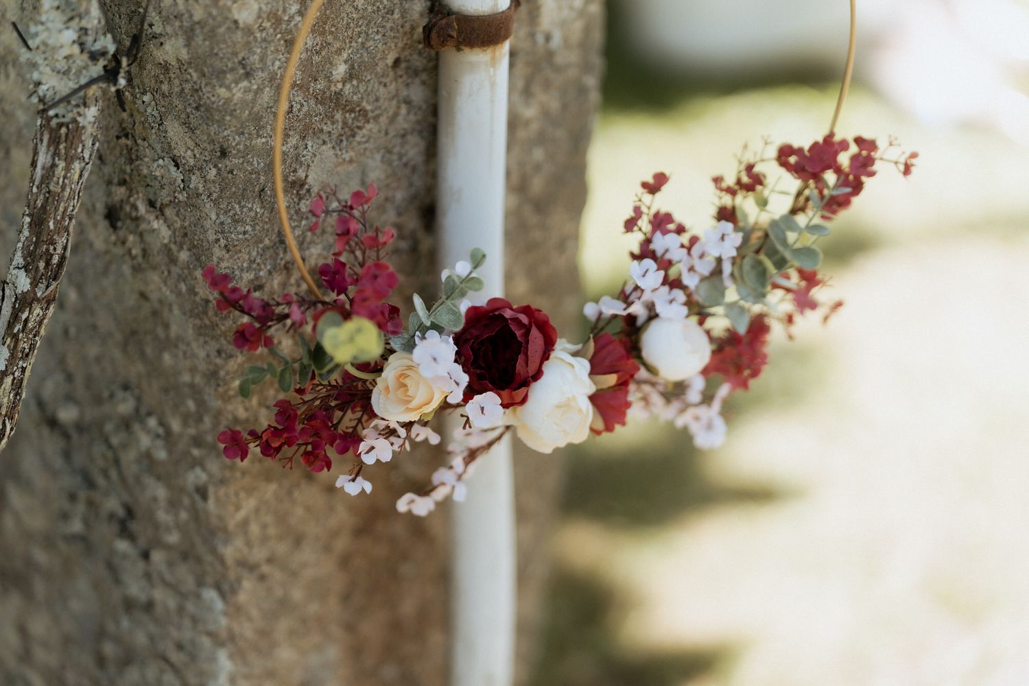 A delicate floral crown with burgundy and cream roses sits against a rustic stone wall backdrop.