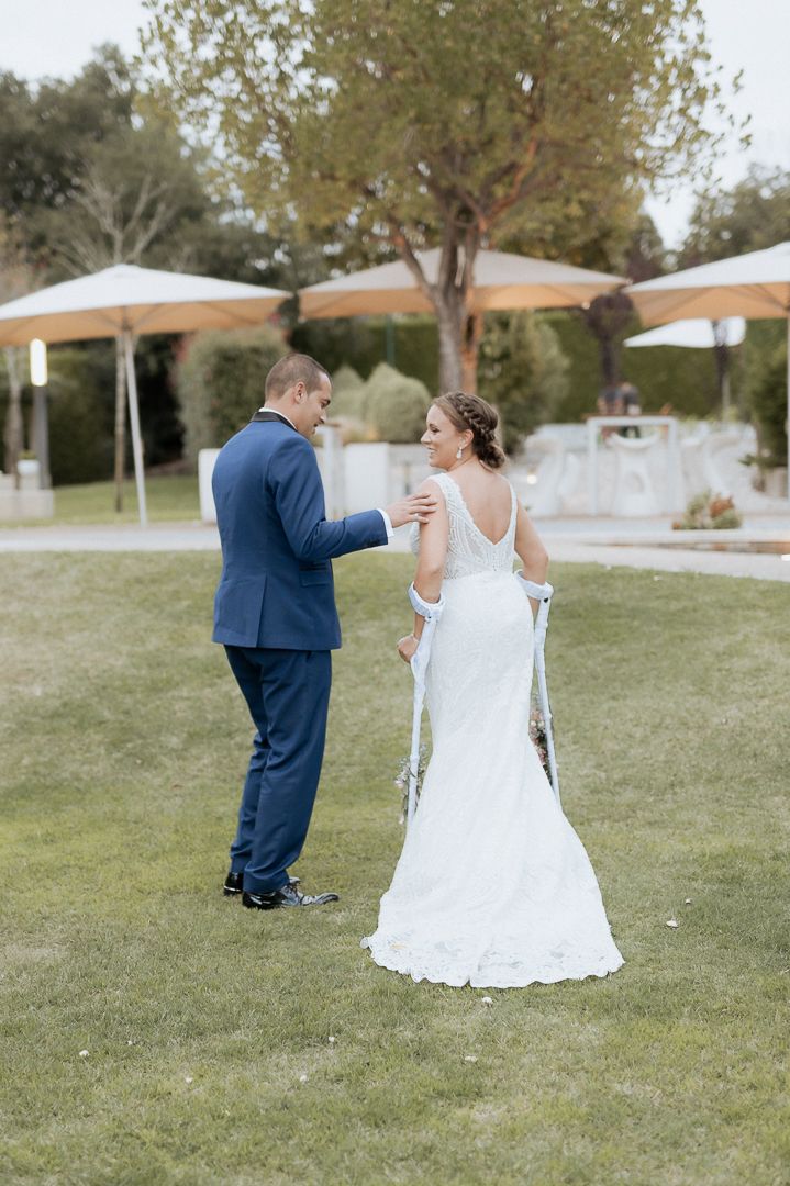 A couple shares a tender moment during their outdoor wedding reception under white canopies and trees.