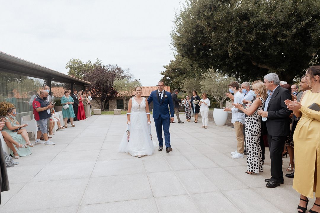 Wedding guests line both sides of an outdoor patio to celebrate as a couple in formal attire walks down the center.