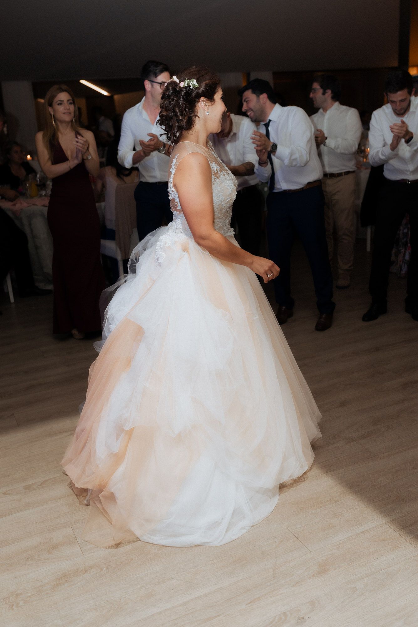 A bride in a white ballgown dances at her wedding reception while guests watch and applaud in the background.