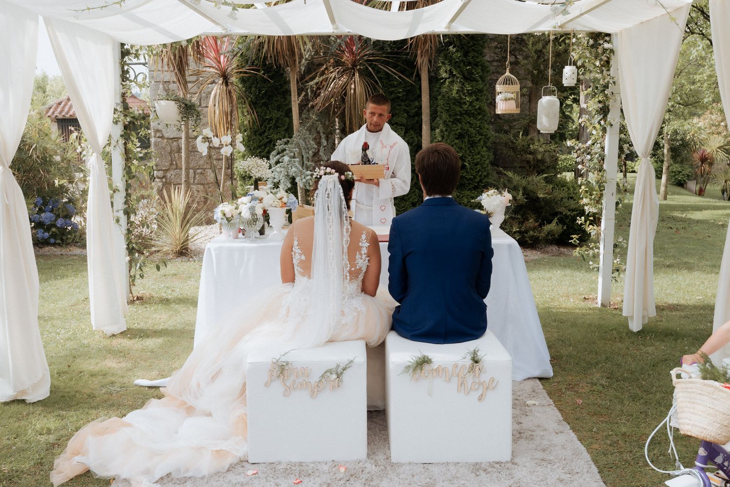 Outdoor wedding ceremony setup with white draped fabric and floral arrangements in a garden setting.