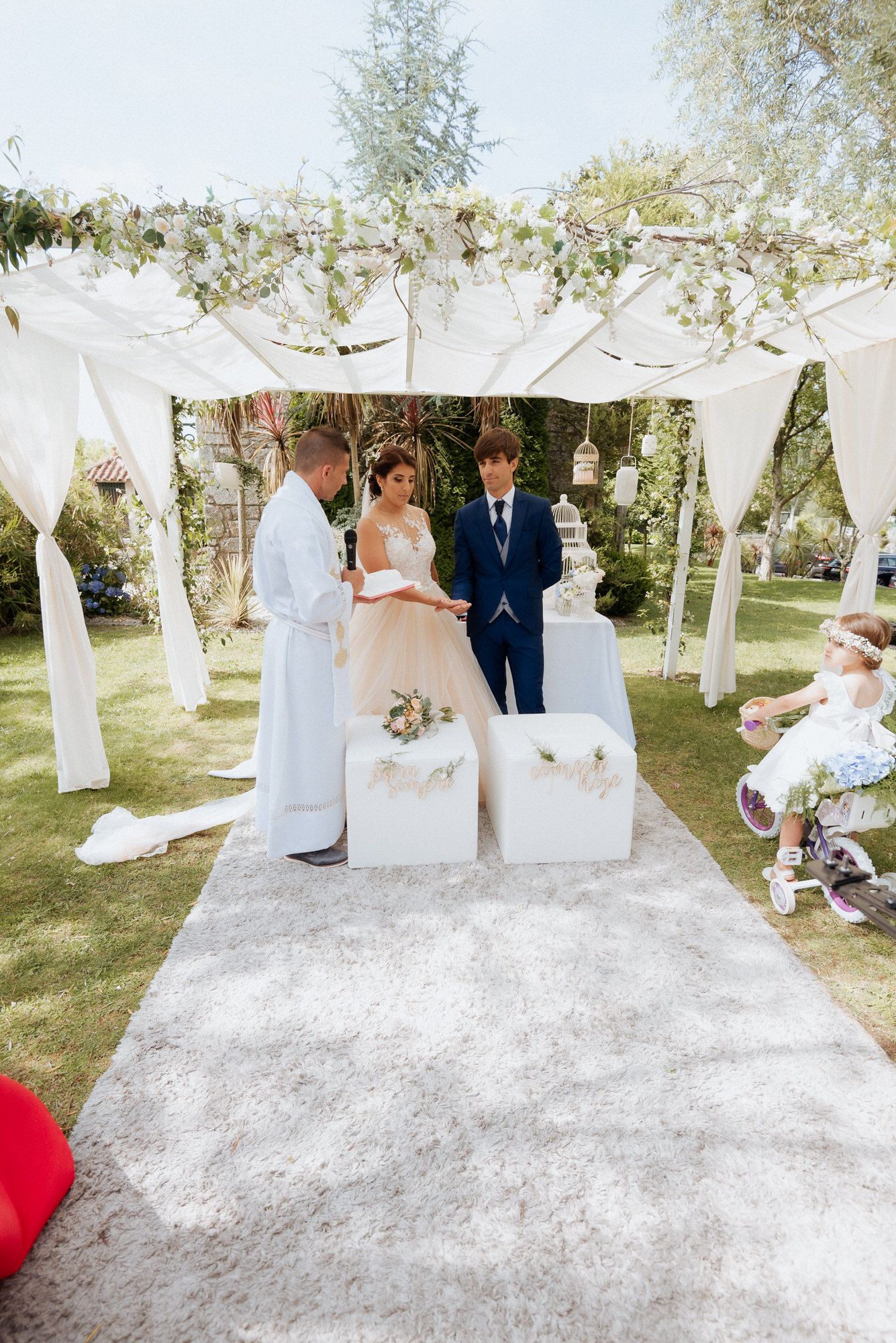 An outdoor wedding ceremony setup with white fabric canopy, floral decorations and elegant decor on a sunny day.