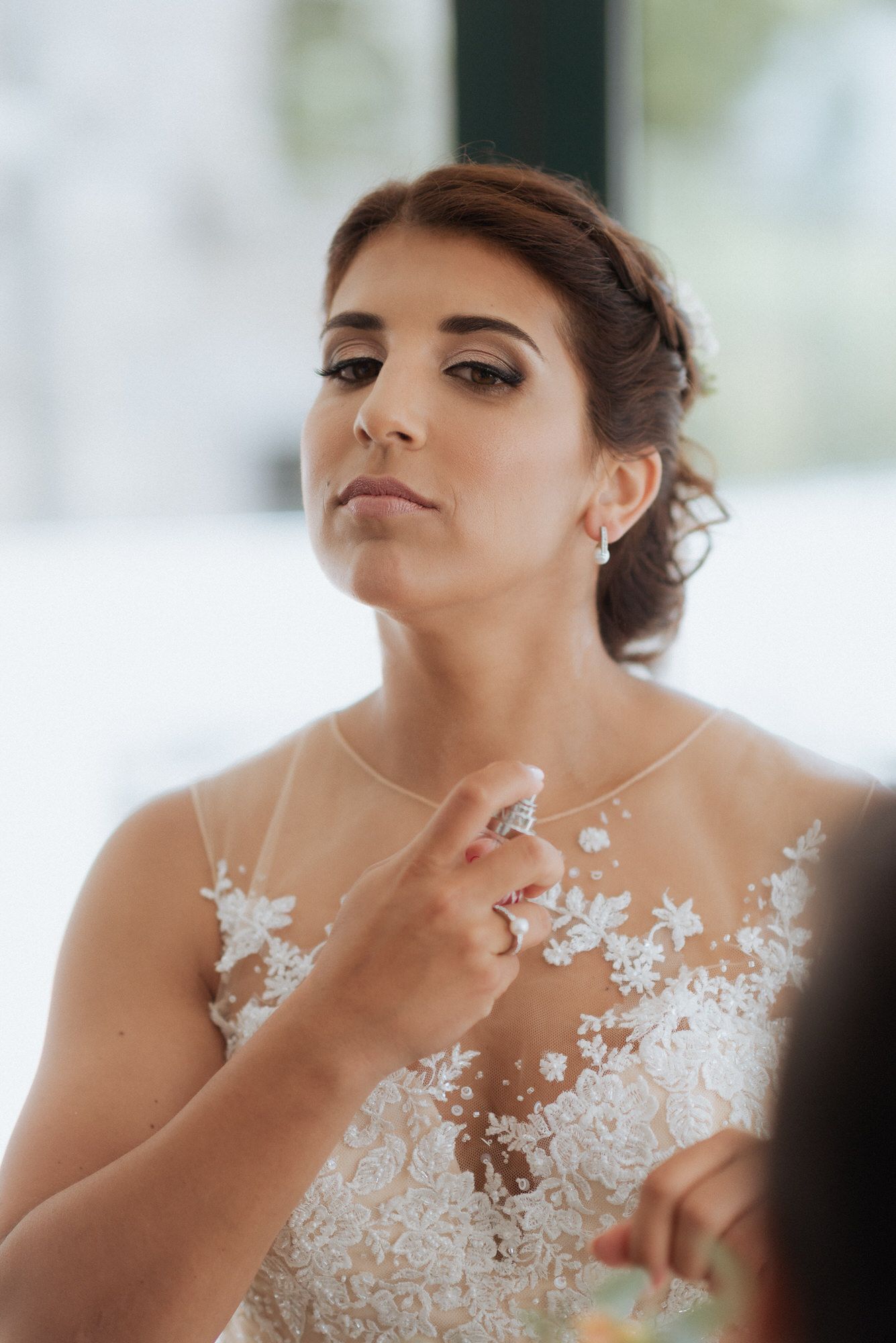 A bride in an elegant white lace wedding dress with delicate floral appliques poses during preparations.