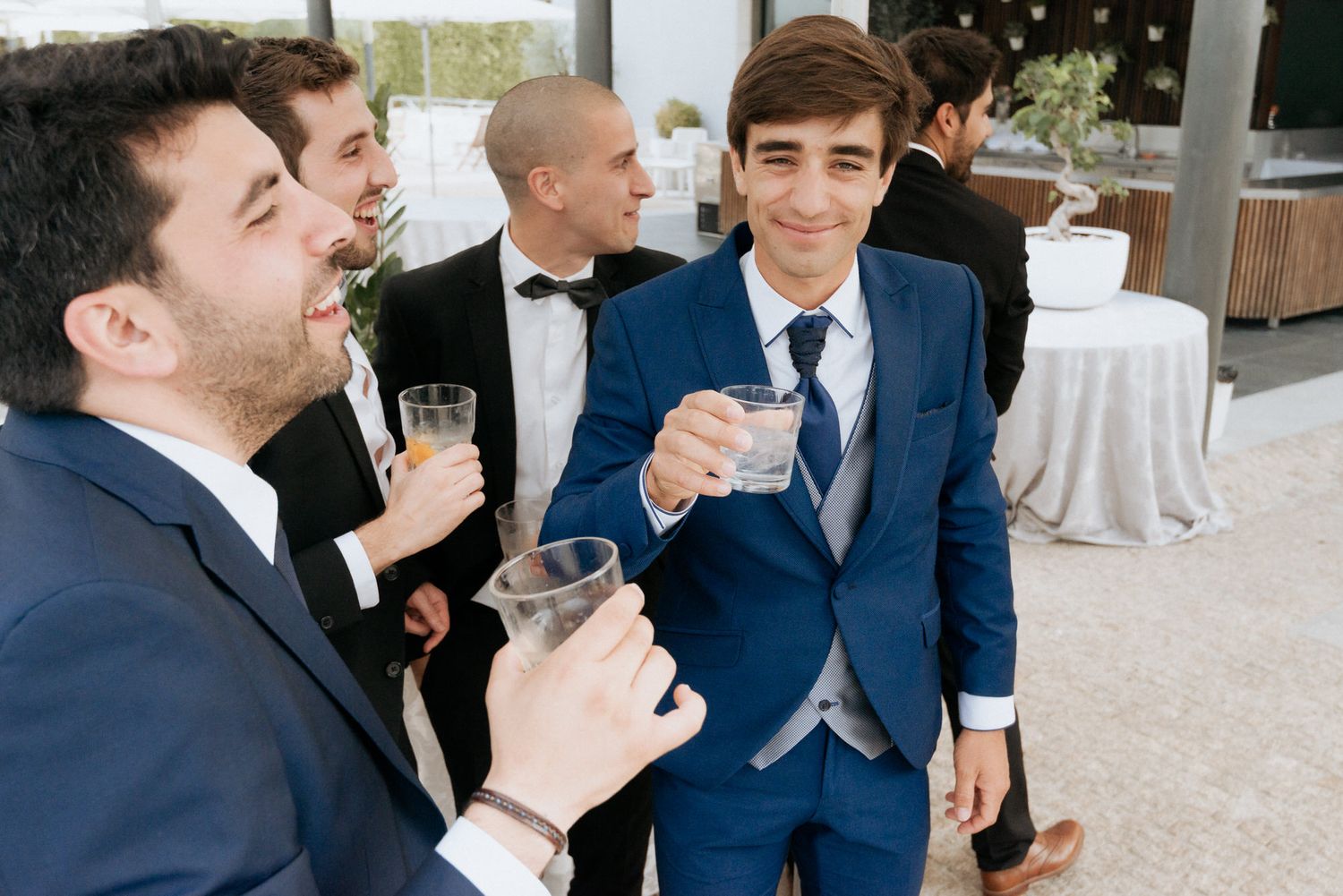 Well-dressed guests in formal suits enjoying drinks at an elegant wedding reception.