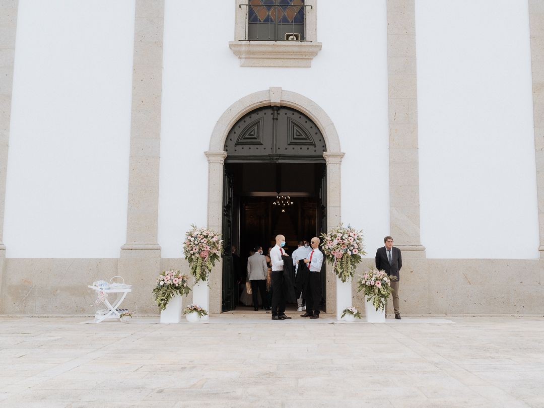 Small group stands in front of a white church entrance adorned with floral arrangements and decorative elements.