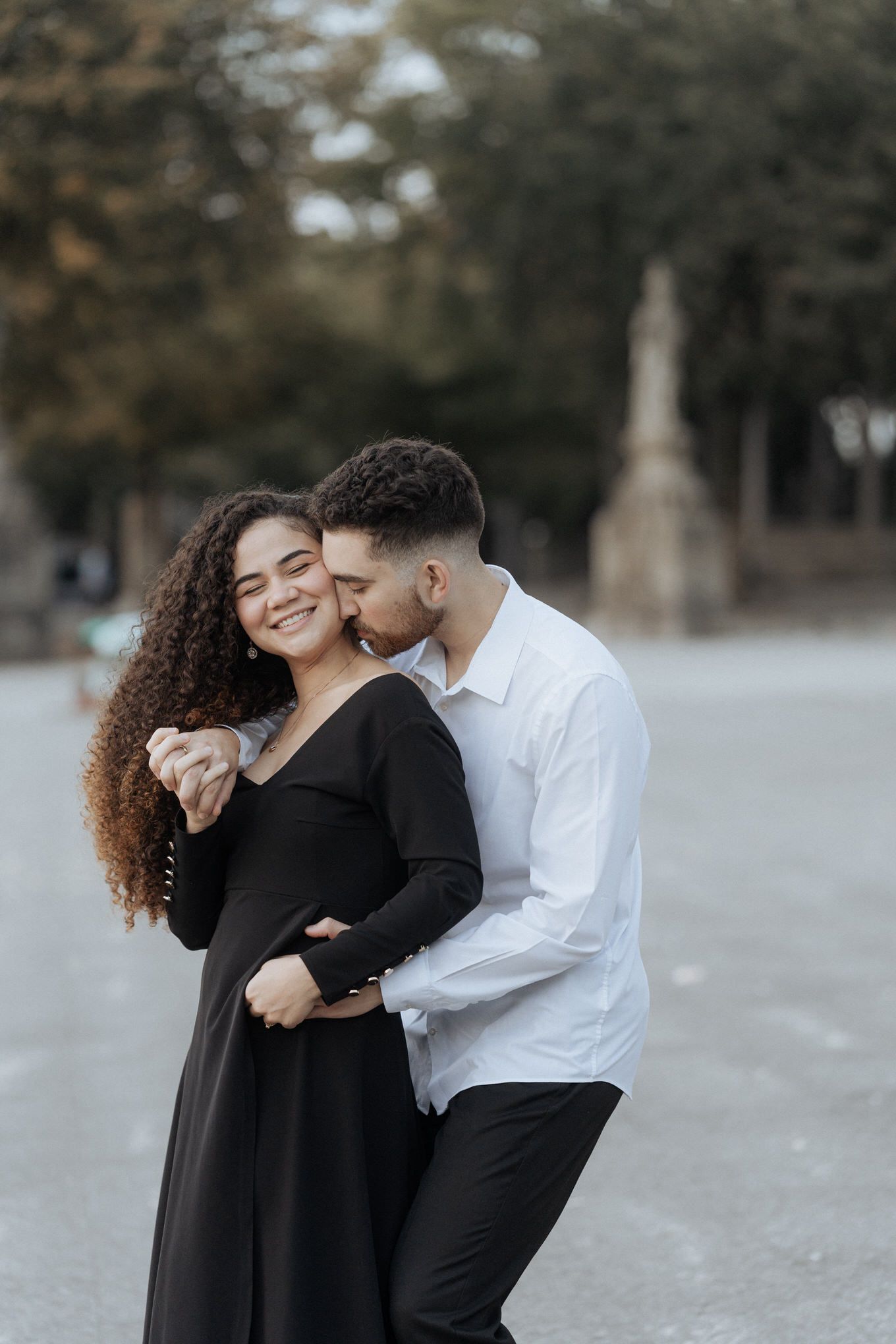 Casal carinhoso em traje formal compartilha momento íntimo enquanto se abraçam ao ar livre.