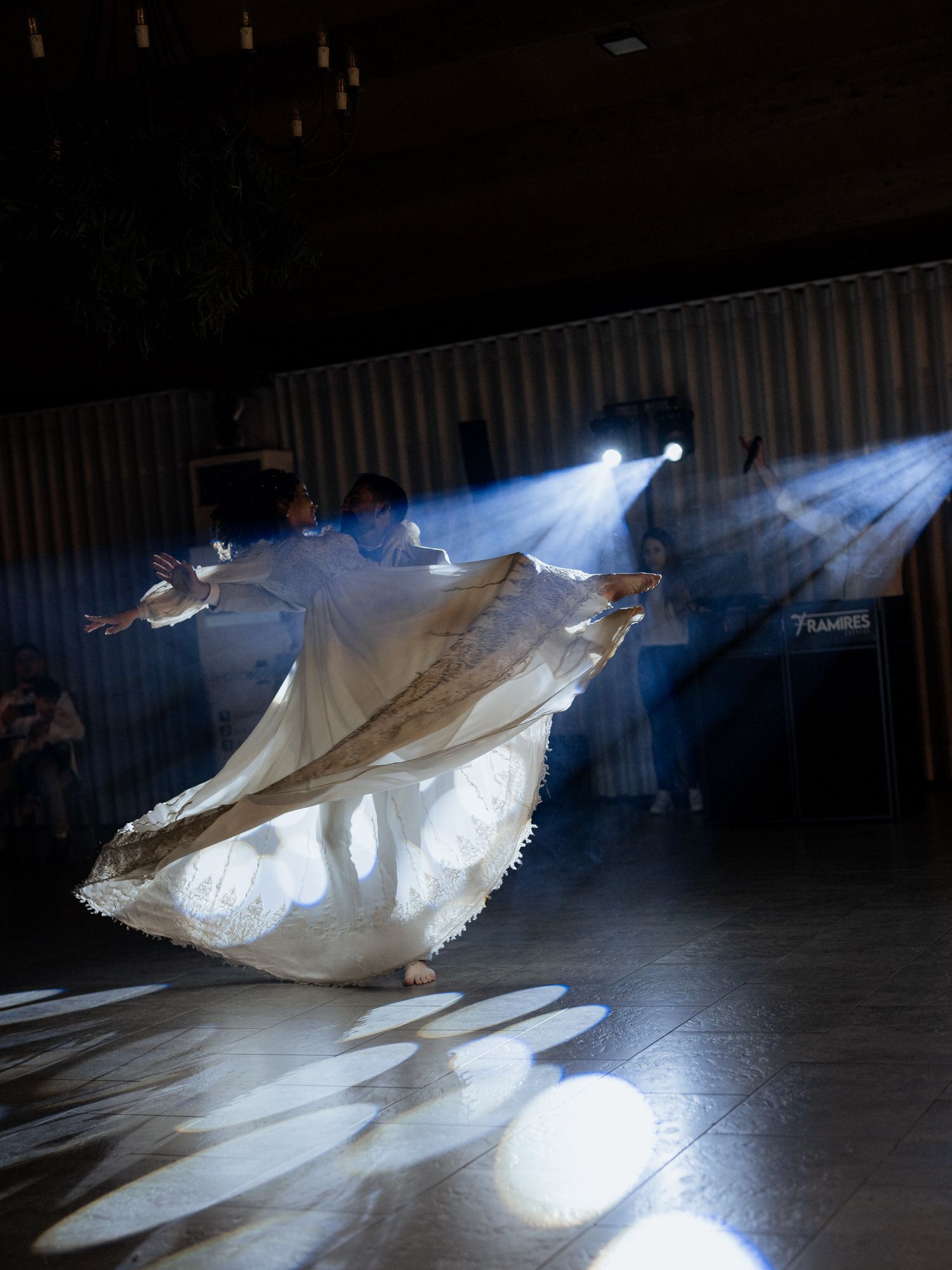 Dancers in flowing white fabric perform under dramatic blue spotlights creating ethereal shadows on stage.