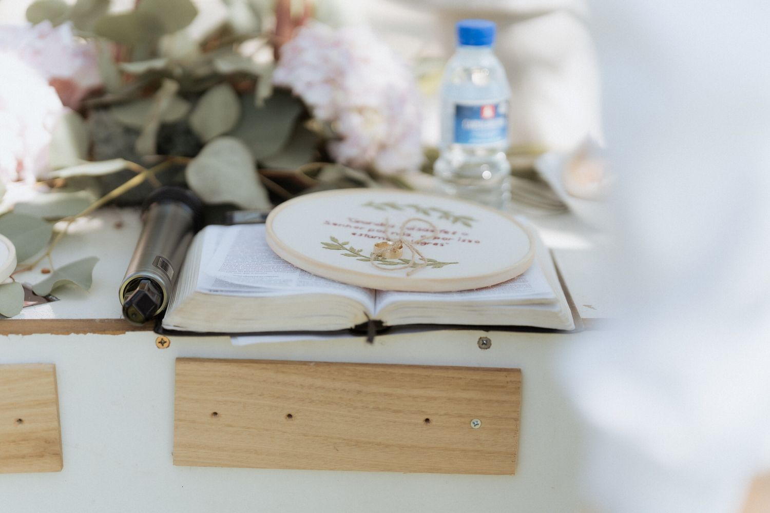 Open book with embroidery design and wooden plank on white surface with floral decorations.