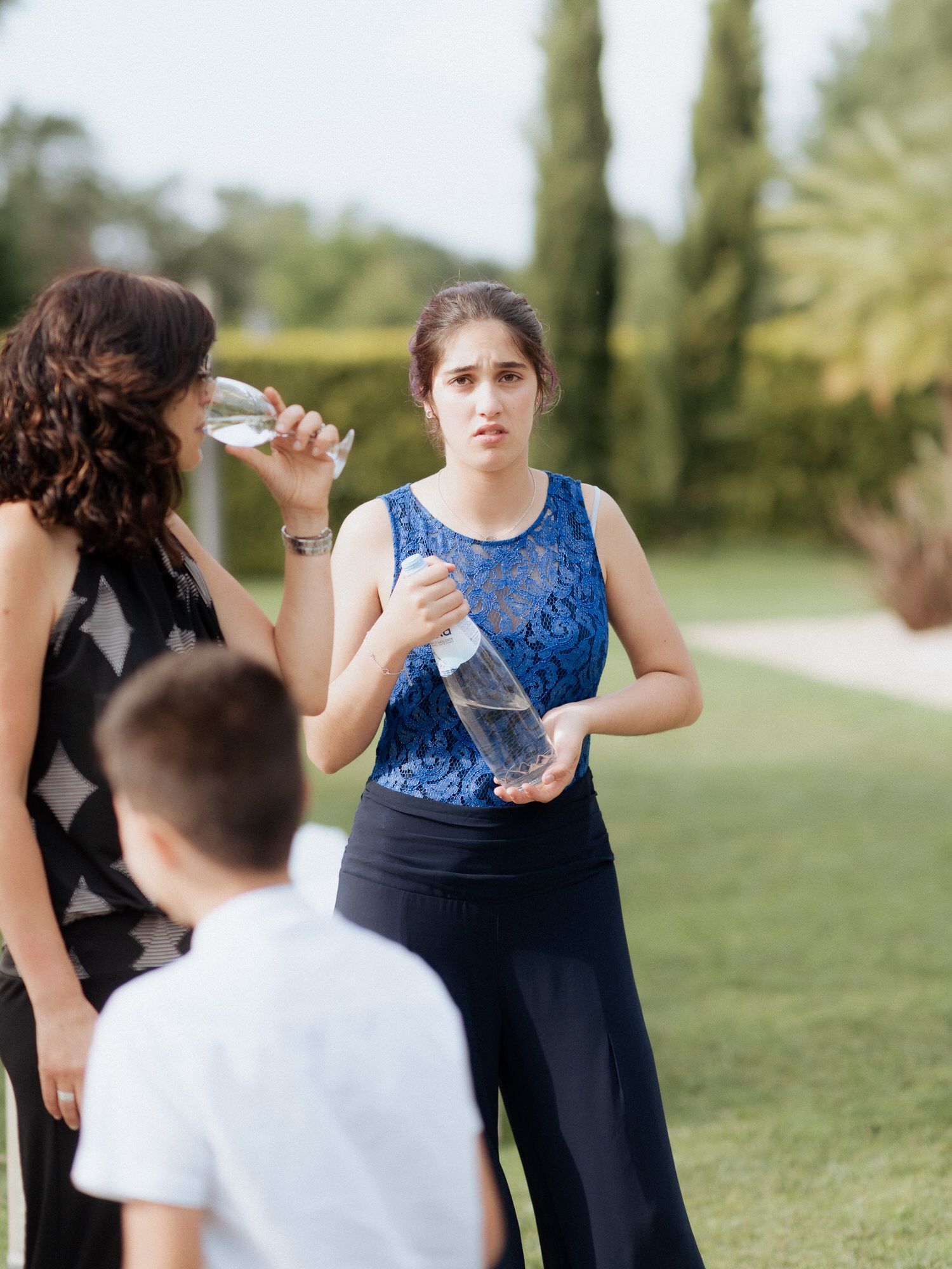A mix of people in formal wear dance and celebrate outdoors on a grassy lawn during a special occasion.