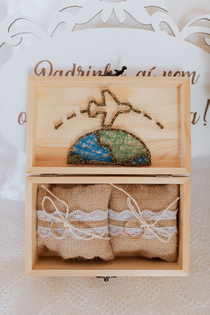 Wooden wedding ring box with decorative world map and airplane design on lid, containing two lace-trimmed burlap pouches.