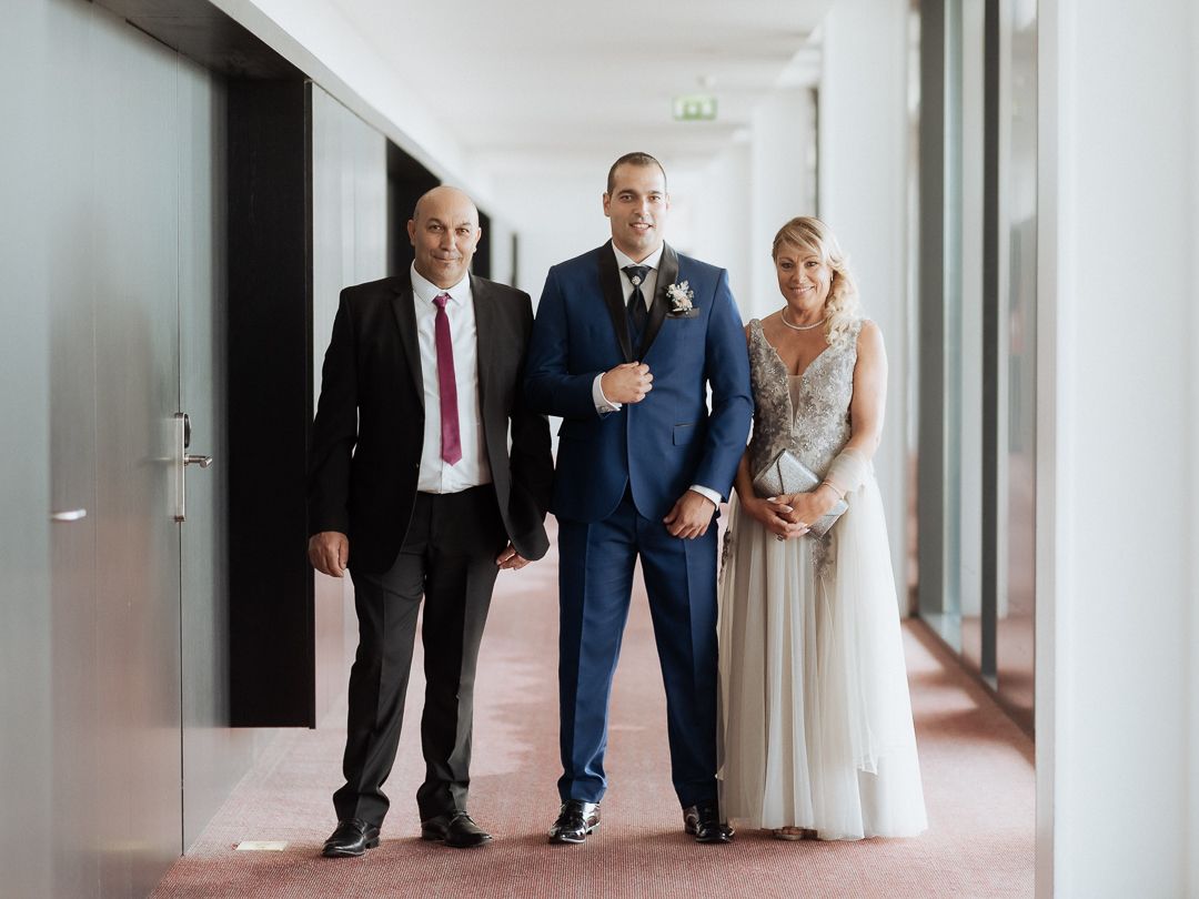 Three people in formal attire including suits and an evening gown standing together in a hallway.