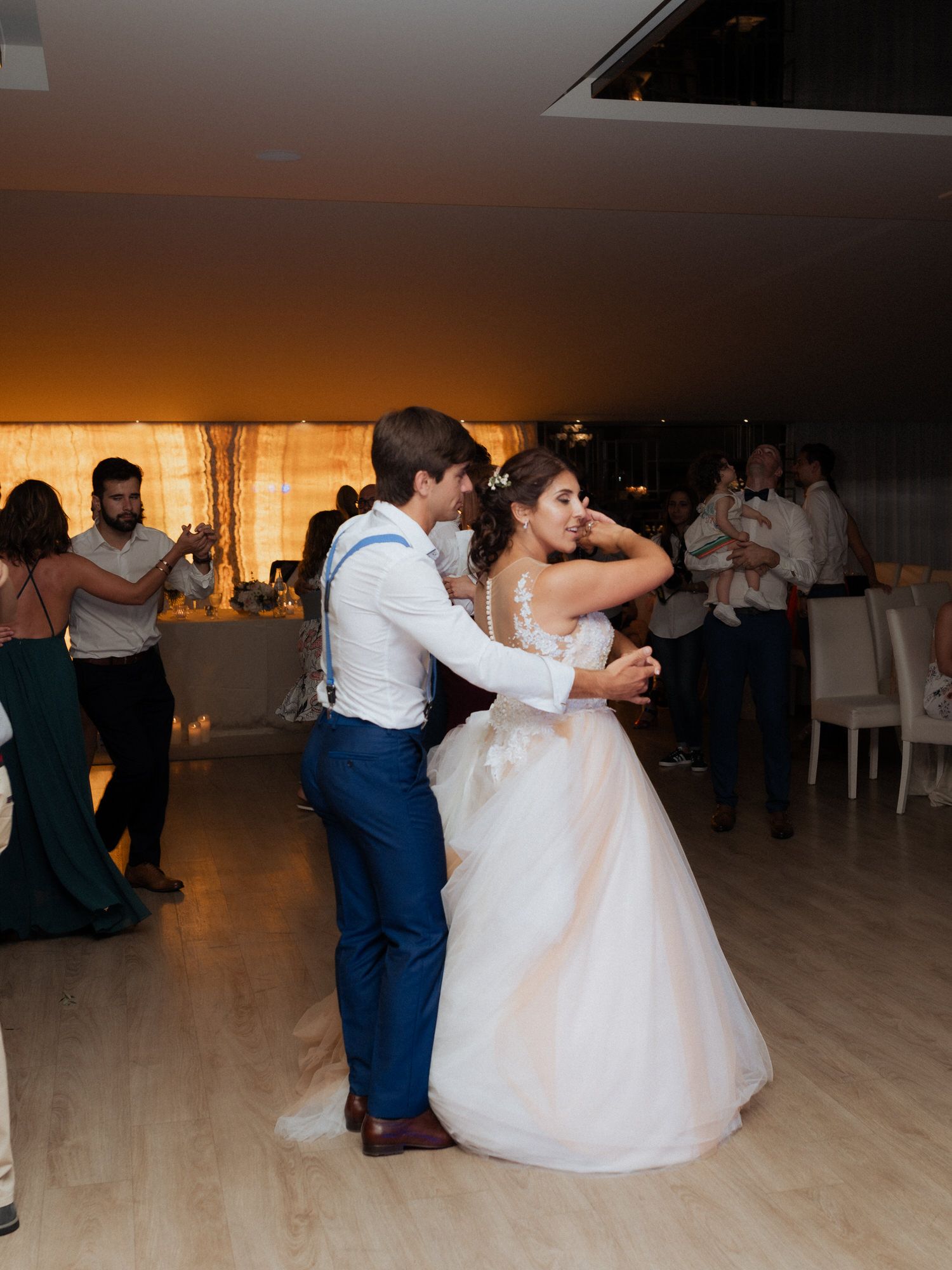 A couple in formal attire dances together at their wedding reception on a light wooden dance floor.