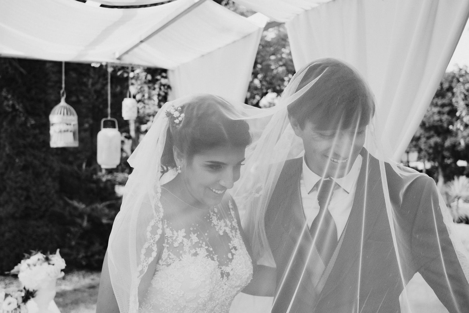Black and white photo of couple under white canopy at outdoor wedding with hanging lantern decorations.