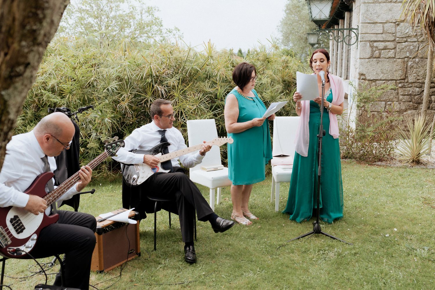 Musicians perform outdoors during an elegant garden event with acoustic guitars and singers in formal attire.