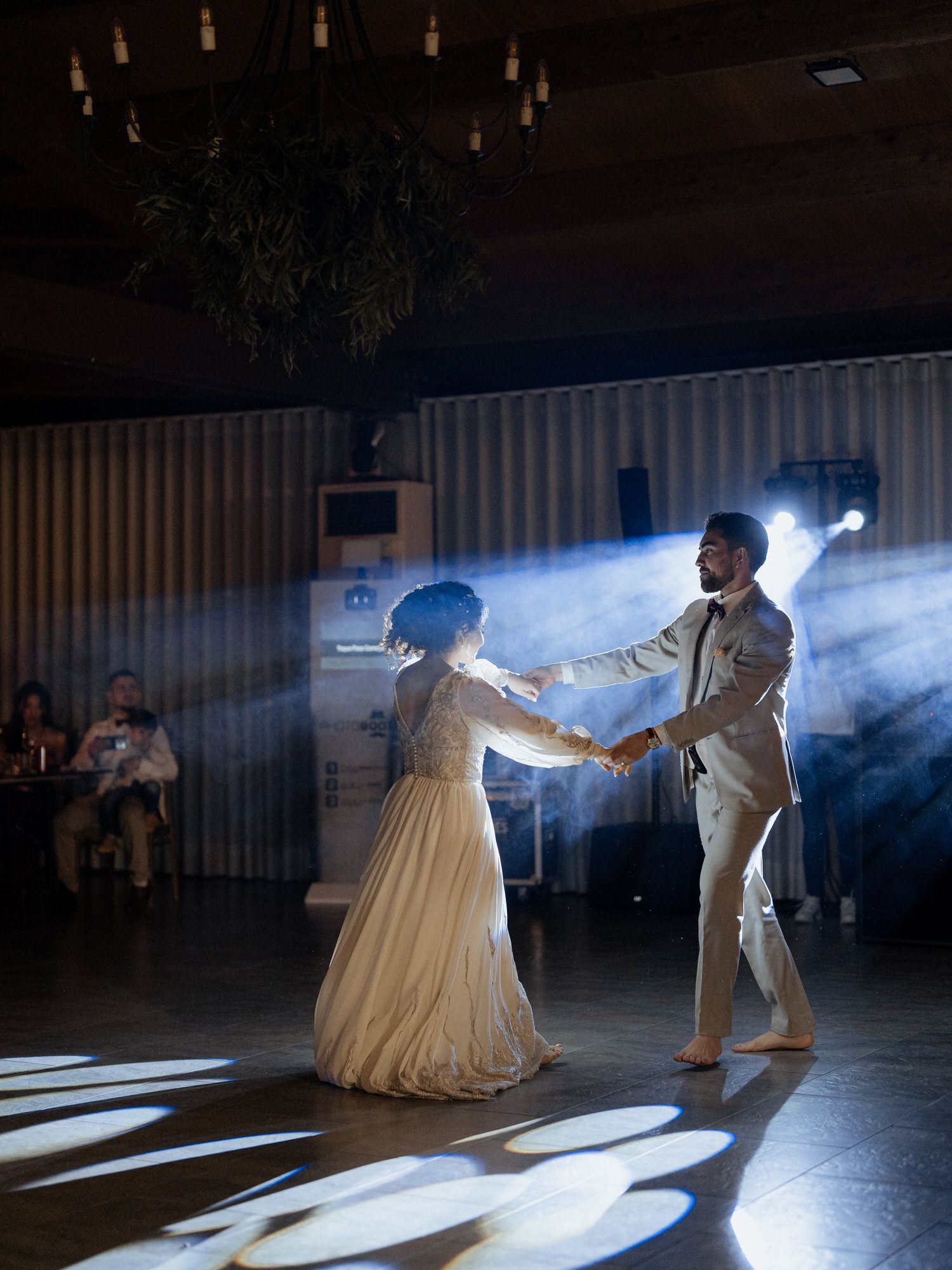 A couple performs their first dance at a wedding reception with atmospheric lighting and smoke effects in the background.